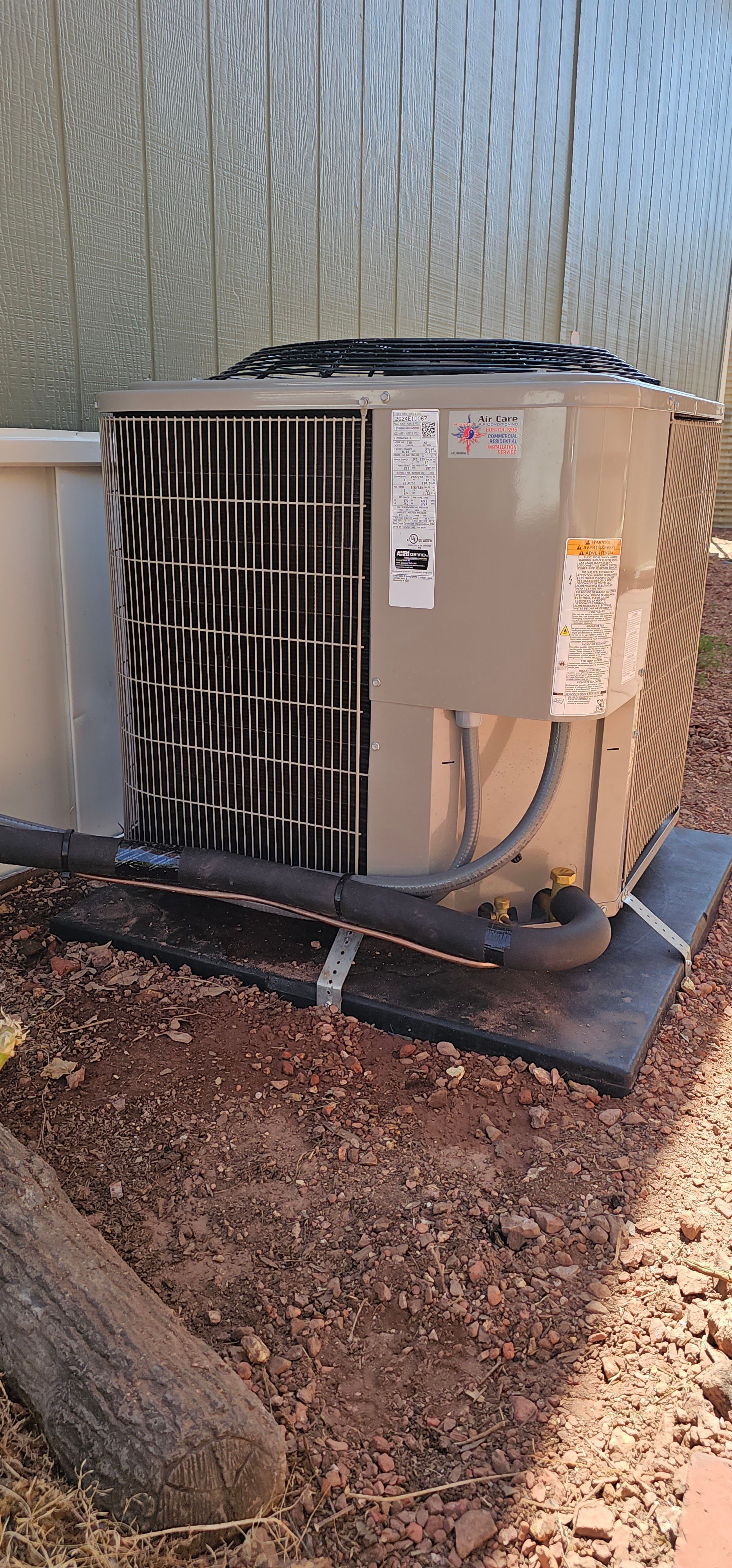 Outdoor HVAC condenser unit beside a house wall on a concrete pad with gravel around it