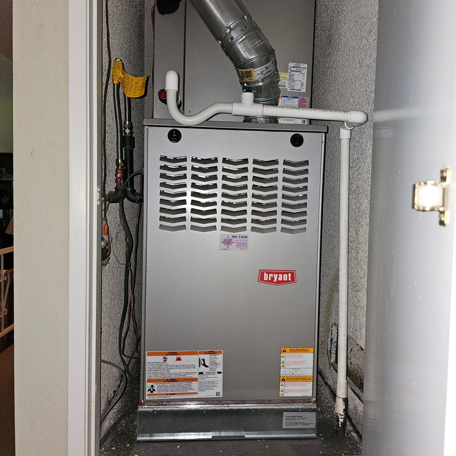 Gray Bryant furnace in a closet, with vent pipes and utility labels visible.