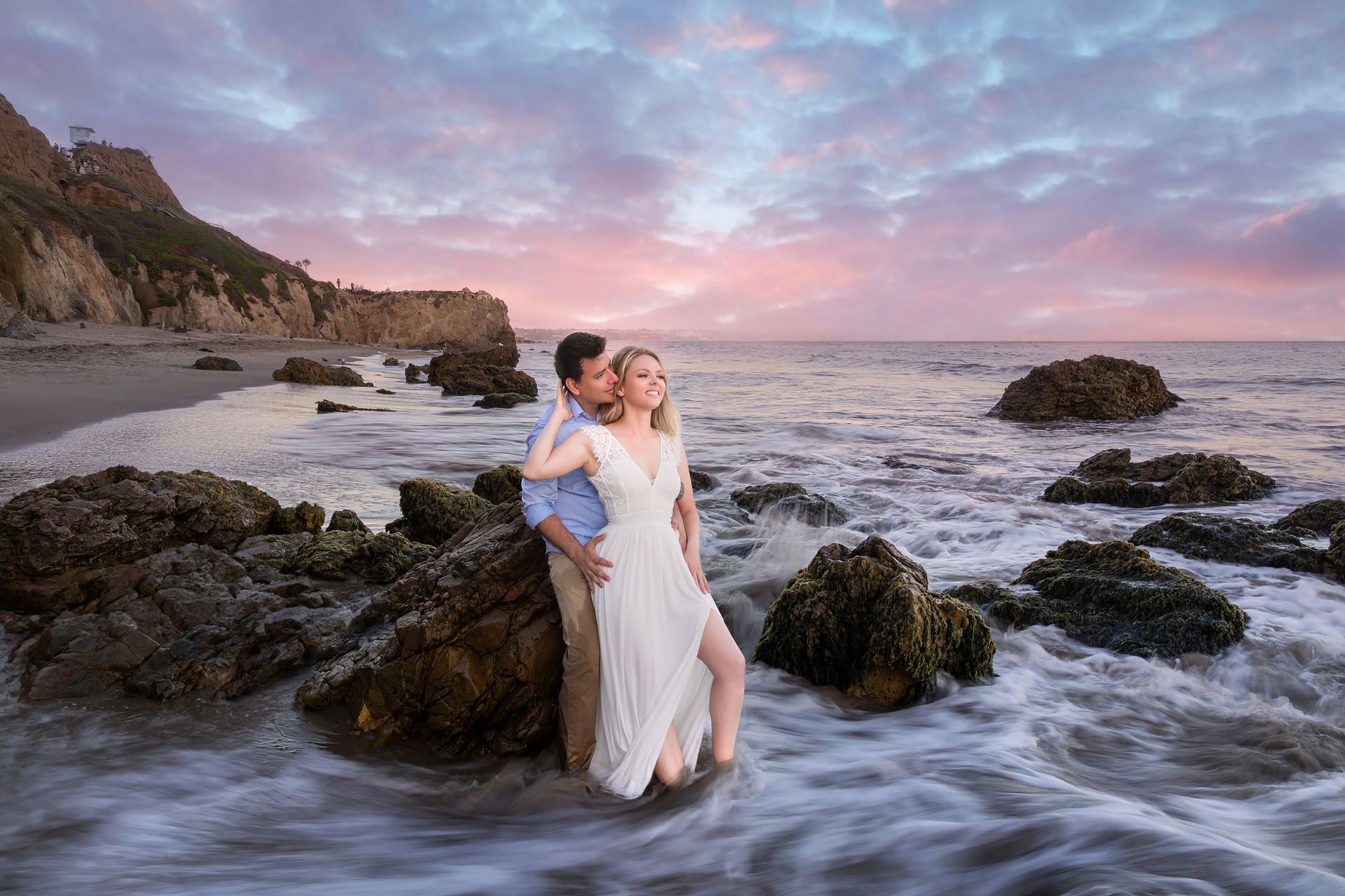 A bride and groom are posing for a picture on the beach.