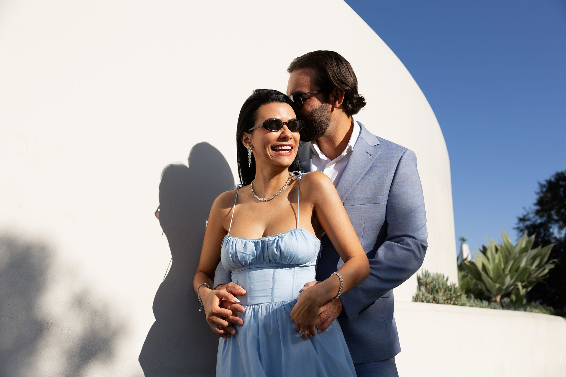 A man and a woman are standing next to each other in front of a white wall.
