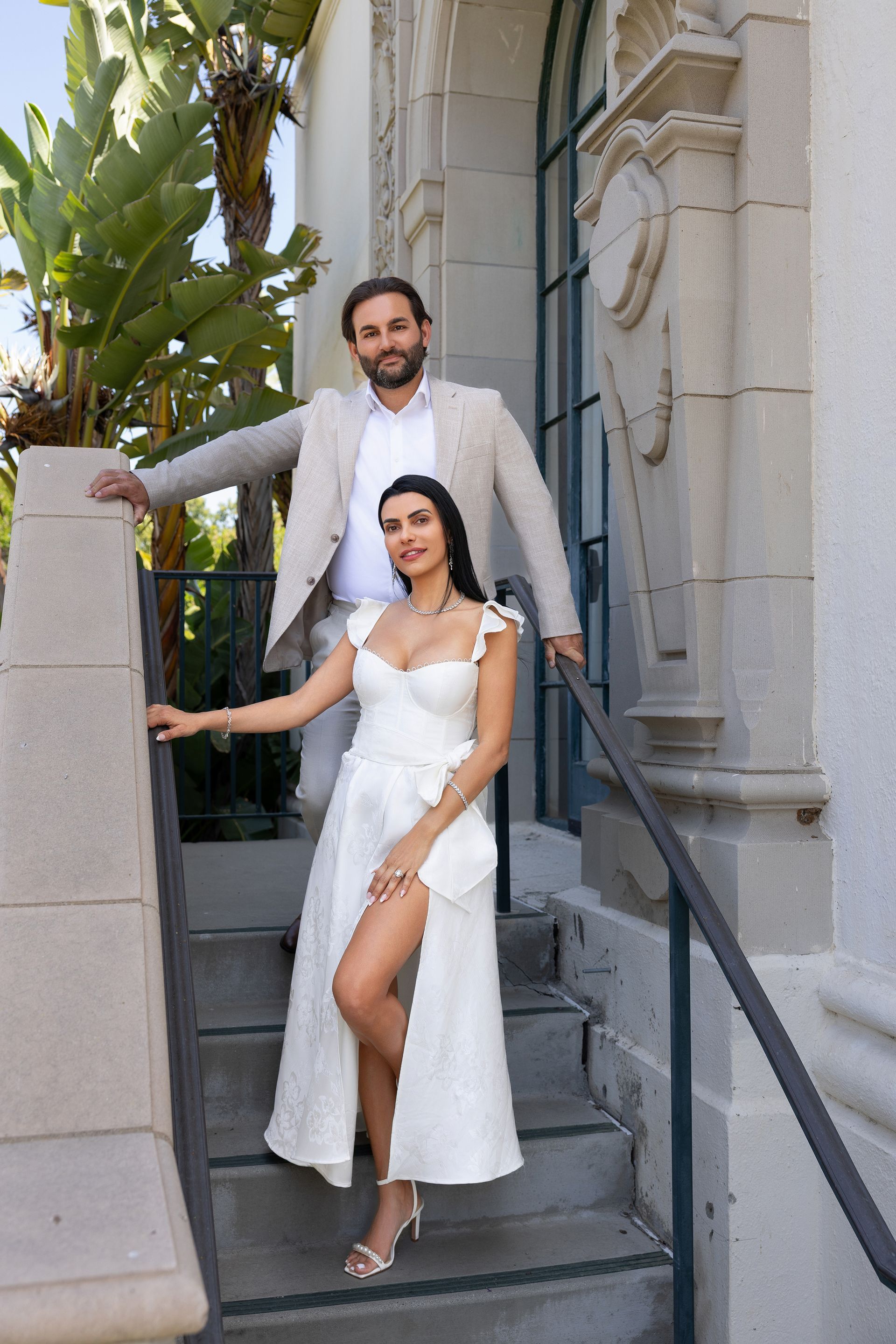 A man and a woman are standing on a set of stairs . the woman is wearing a white dress.