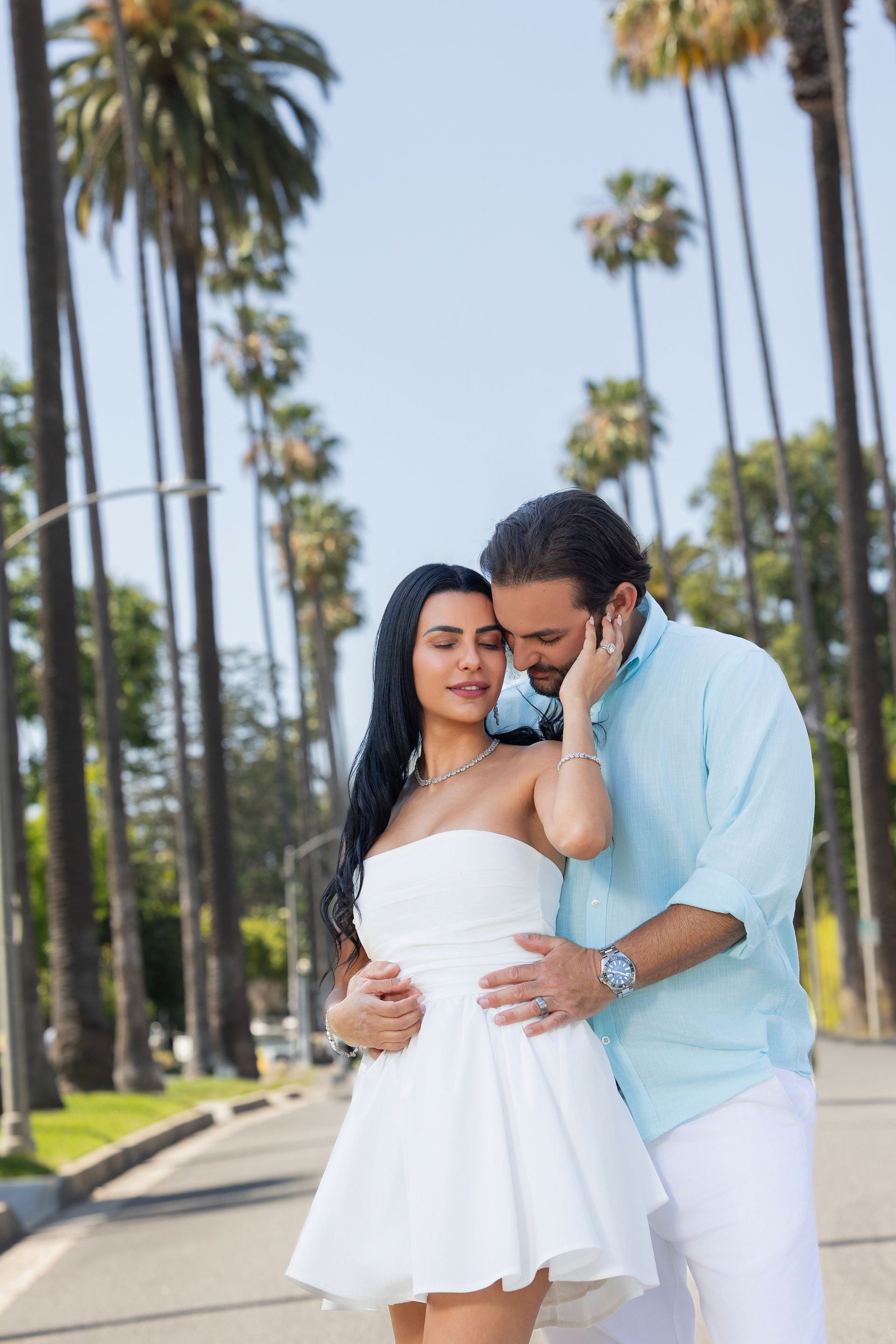 A man and a woman are posing for a picture in front of palm trees.
