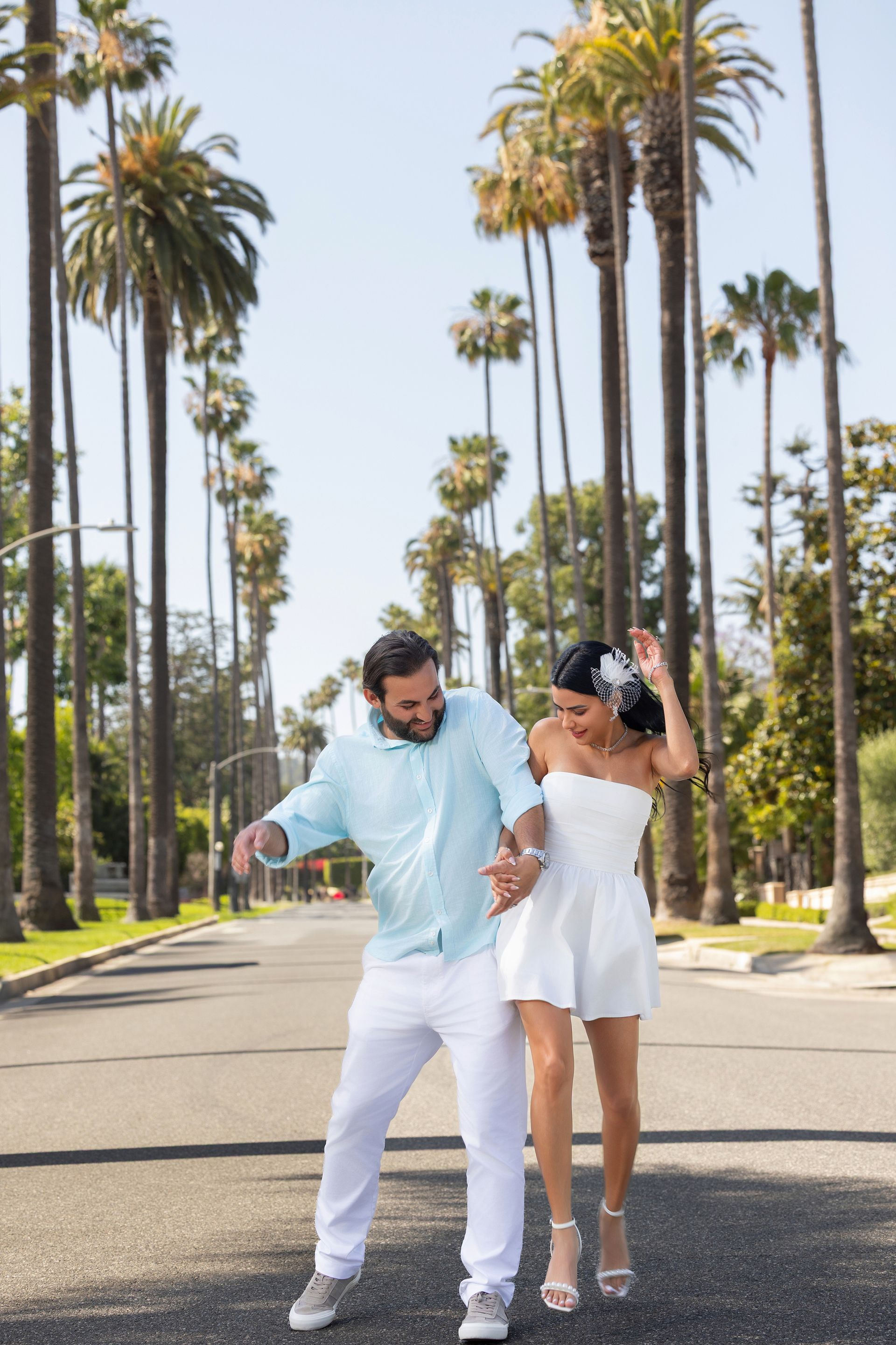 A man and a woman are walking down a street with palm trees in the background.