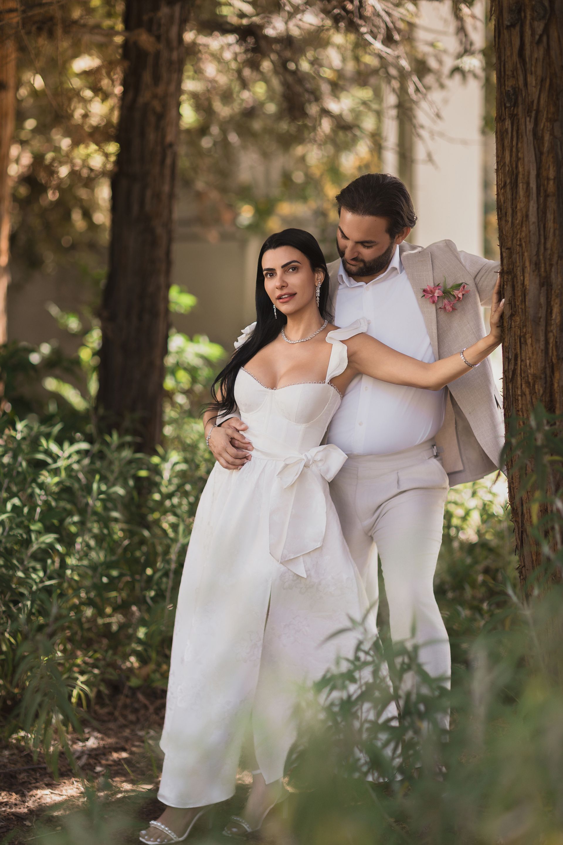 A bride and groom are standing next to each other in the woods.