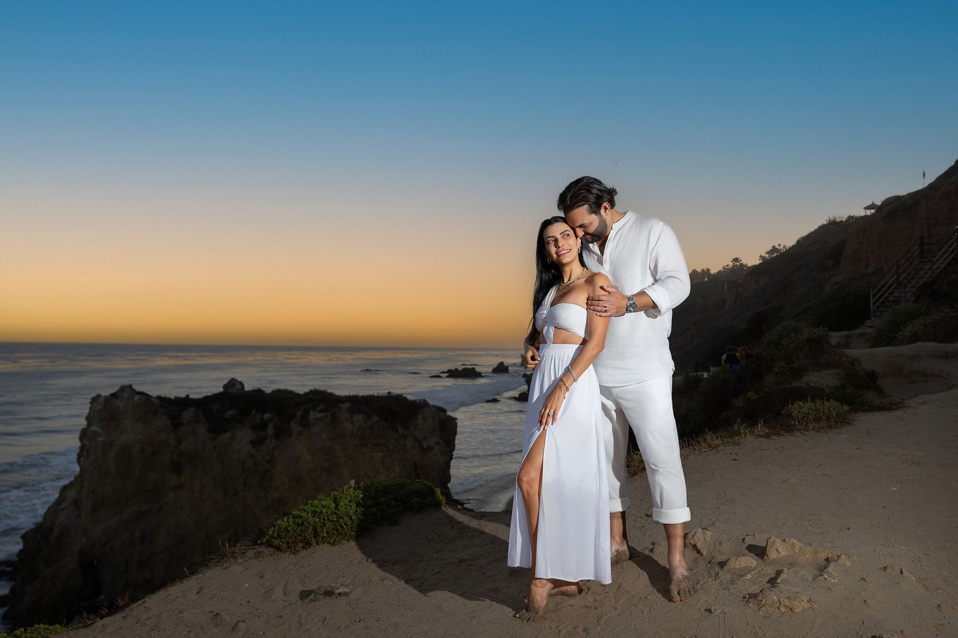 A man and a woman are standing on a beach at sunset.