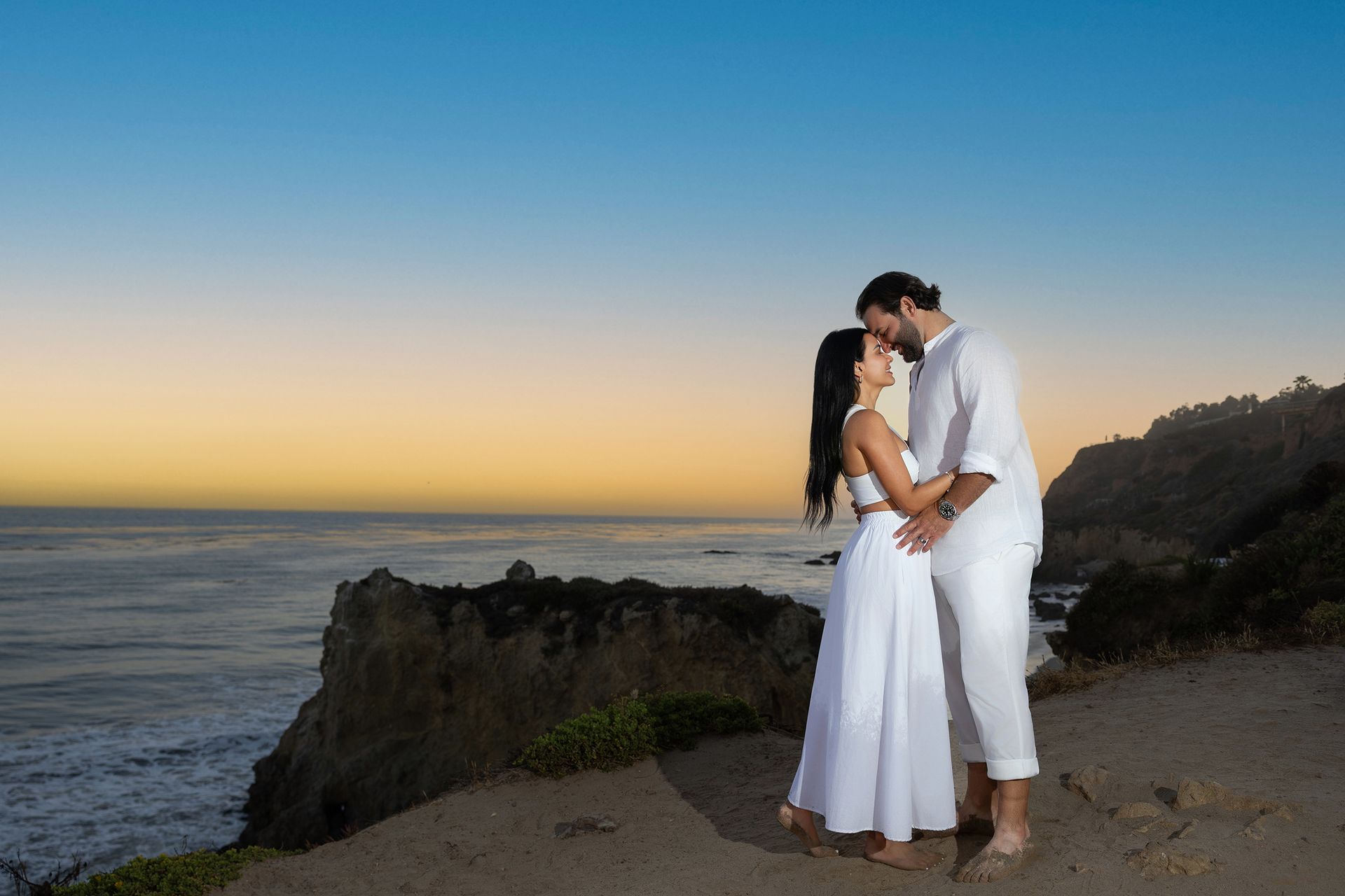 A man and a woman are kissing on the beach at sunset.