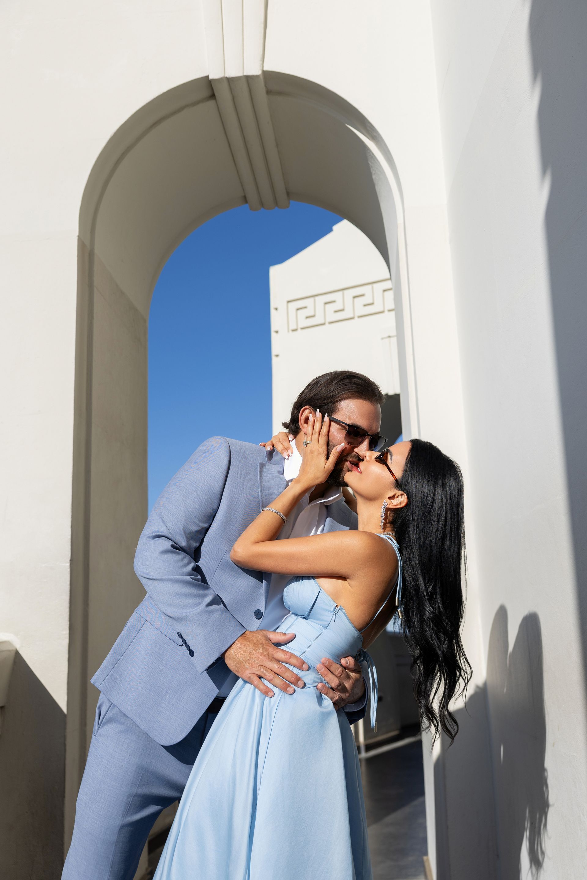 A man in a suit is kissing a woman in a light blue dress.