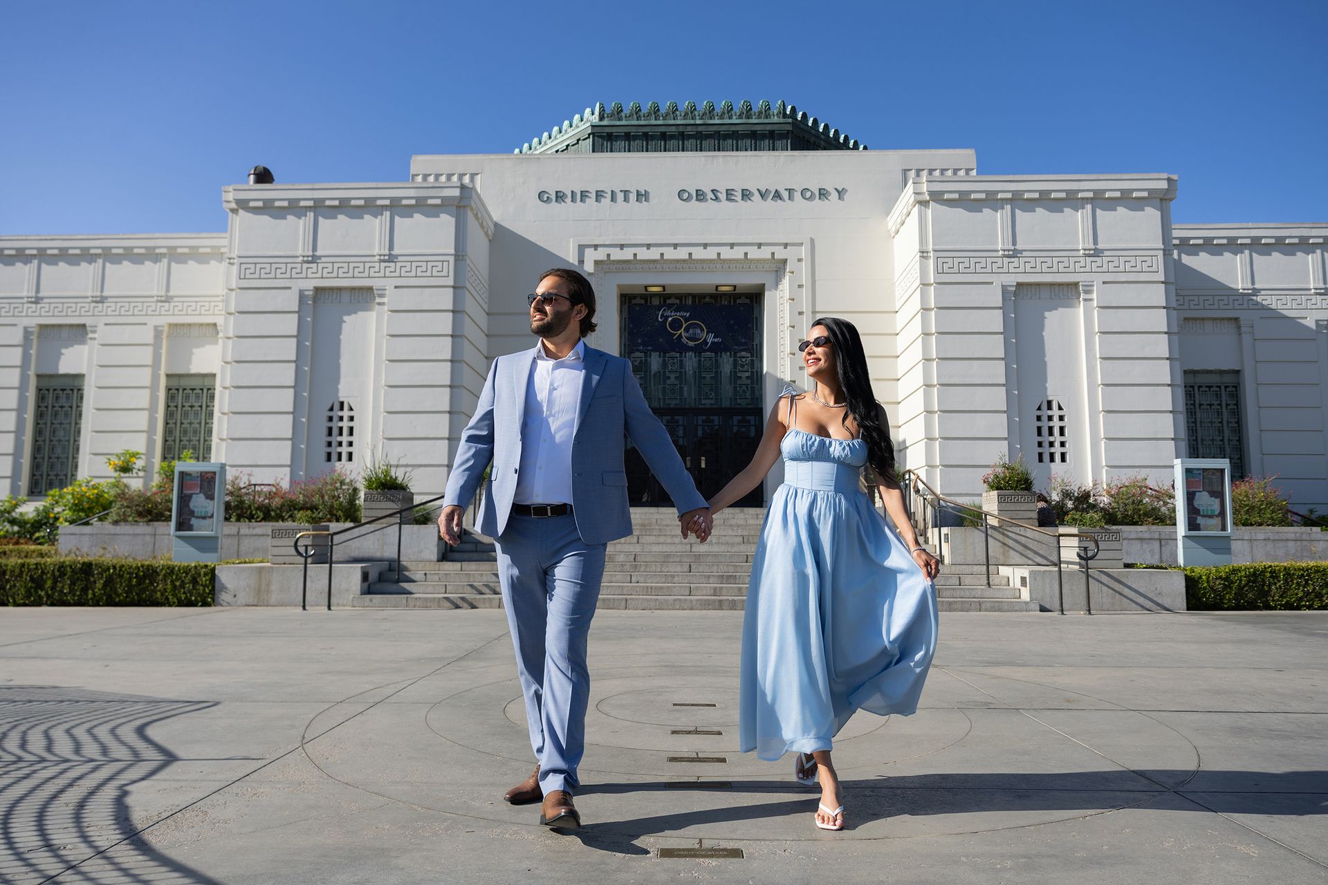 A man and a woman are walking in front of a building holding hands.