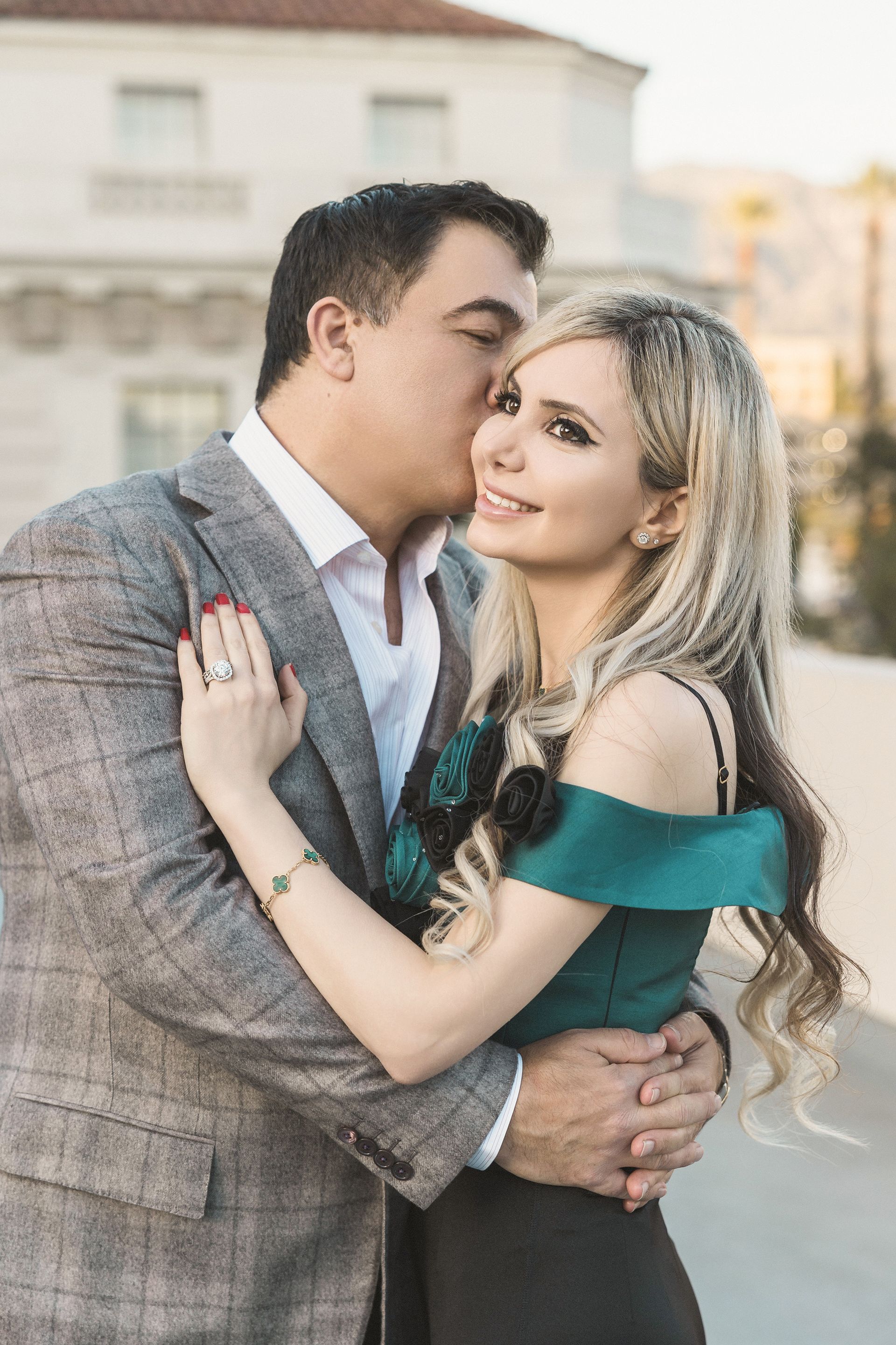 Dad leans in to kiss Mom on the side of her cheek while they stand near the beautiful columns of Pasadena City Hall. The architecture frames the moment, highlighting their affection in a soft and timeless way