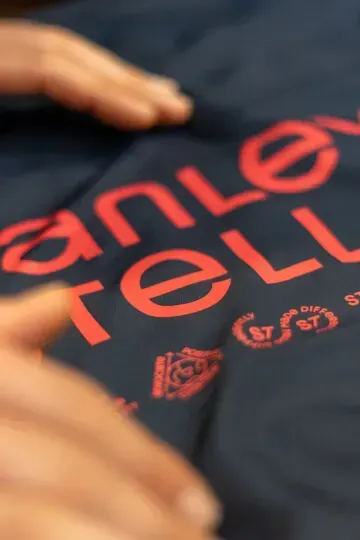Gros plan sur des mains touchant un tissu foncé orné d'inscriptions rouges façon pochoir et de petits logos circulaires.