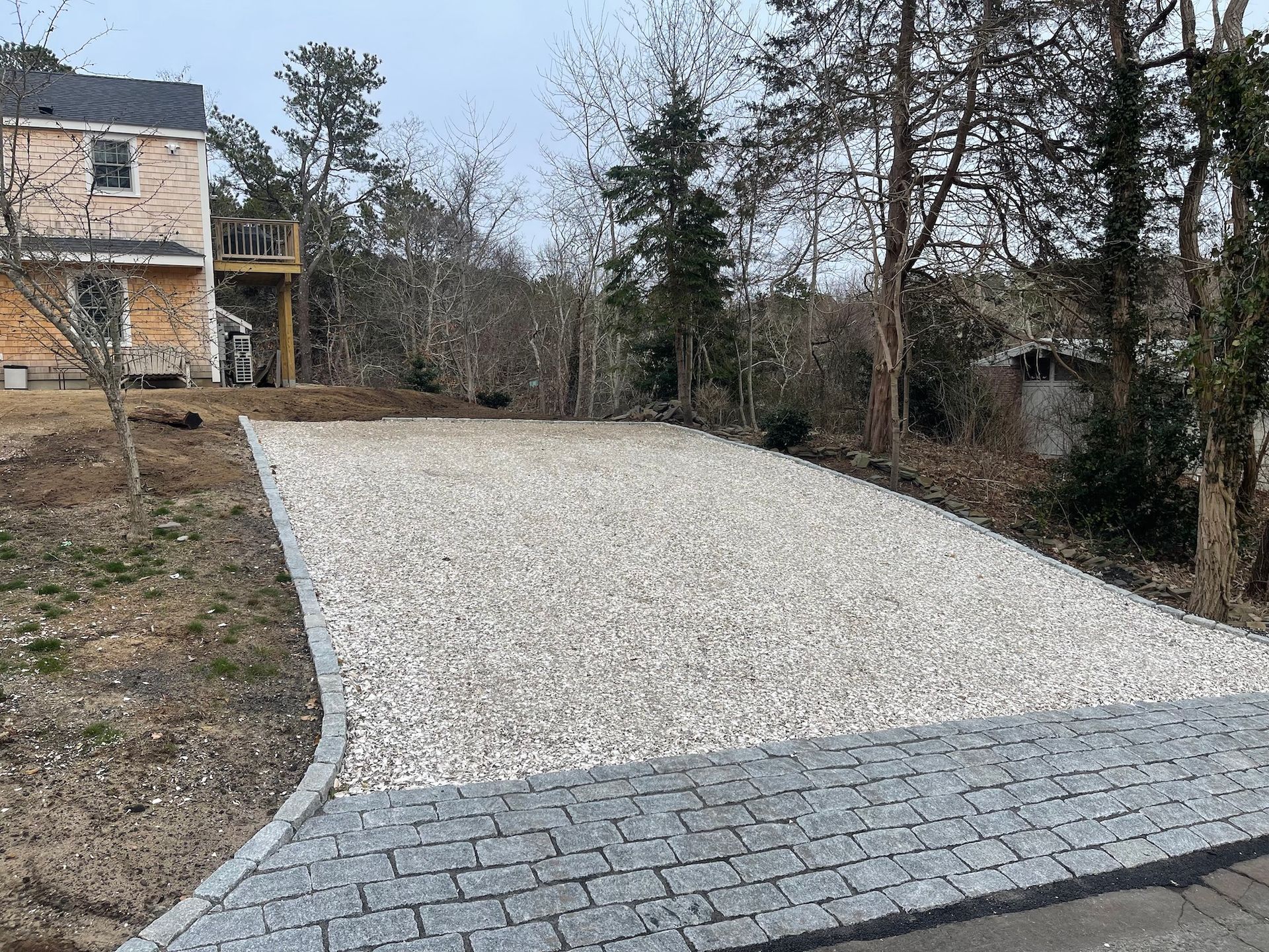 A gravel driveway leading to a house with trees in the background.
