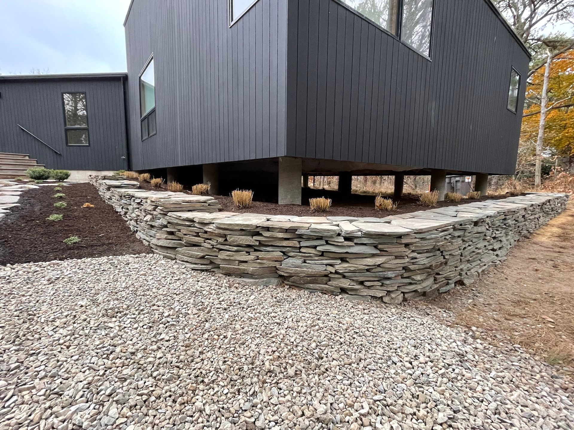 A large black house with a stone wall in front of it.