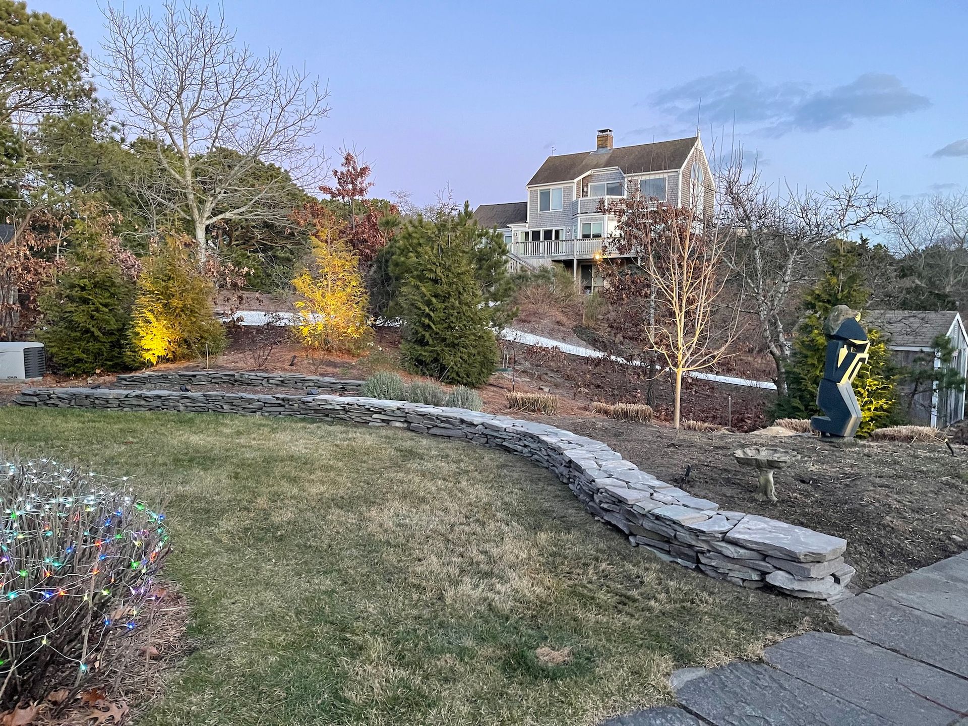 There is a large house in the background and a stone wall in the foreground.