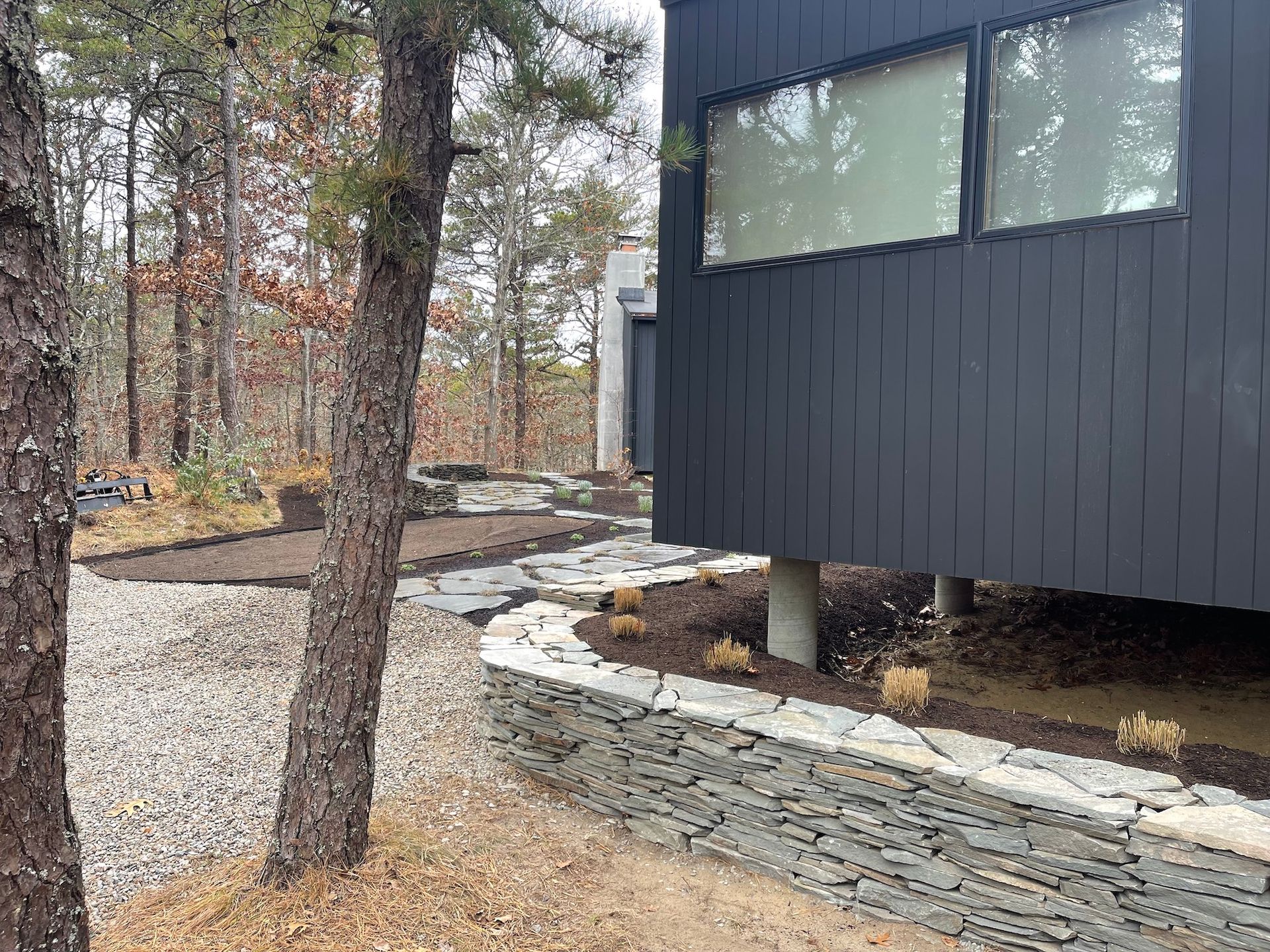 A black house is surrounded by trees and a stone wall.