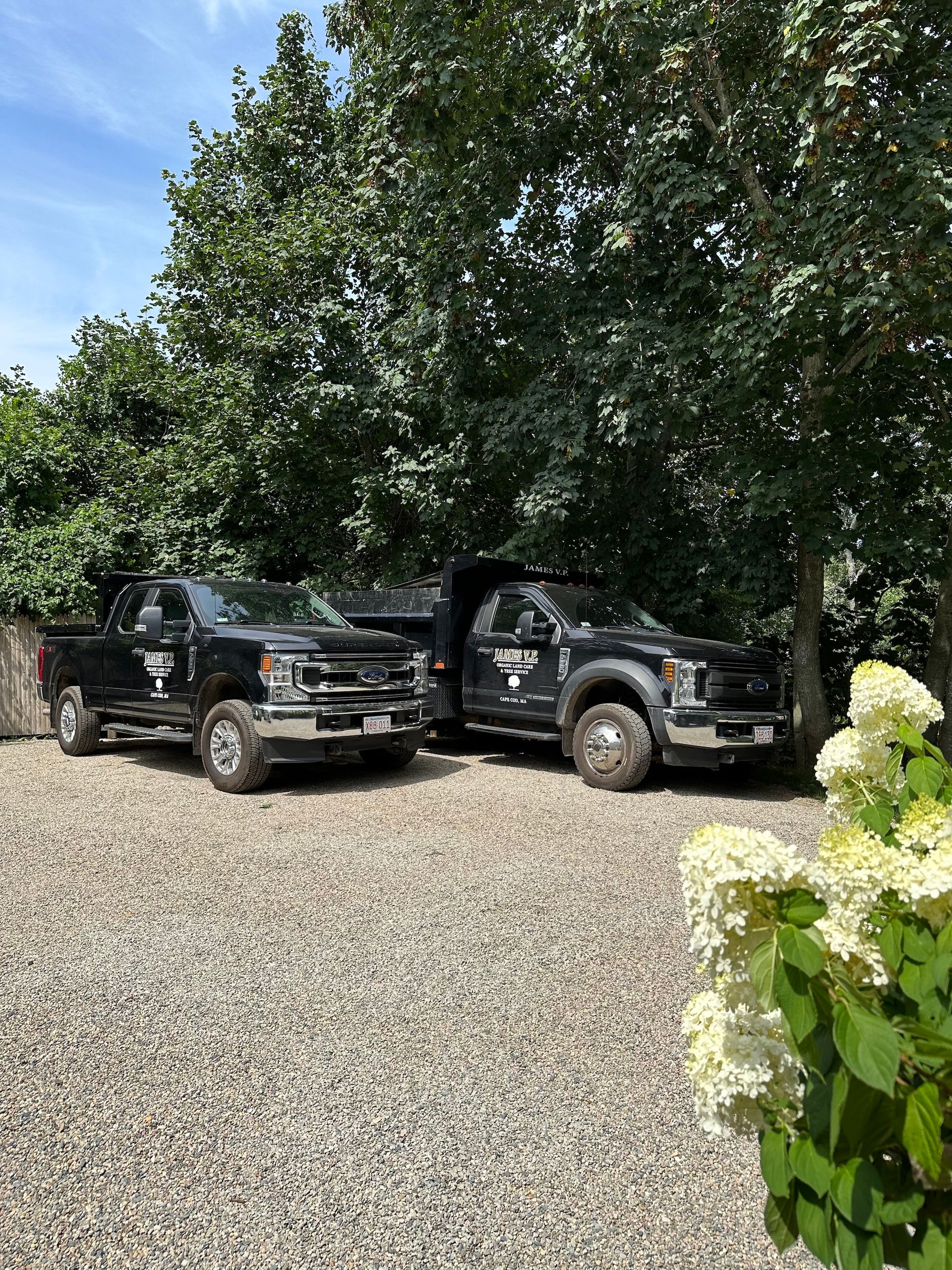 Two black trucks are parked next to each other in a gravel driveway.