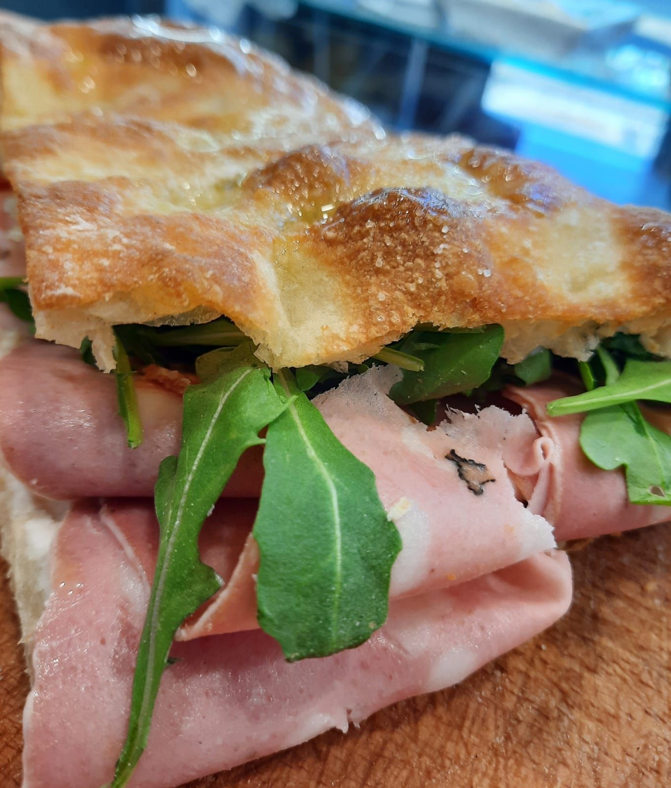 Una focaccia farcita con fette di mortadella e rucola fresca, servita su un tagliere di legno.