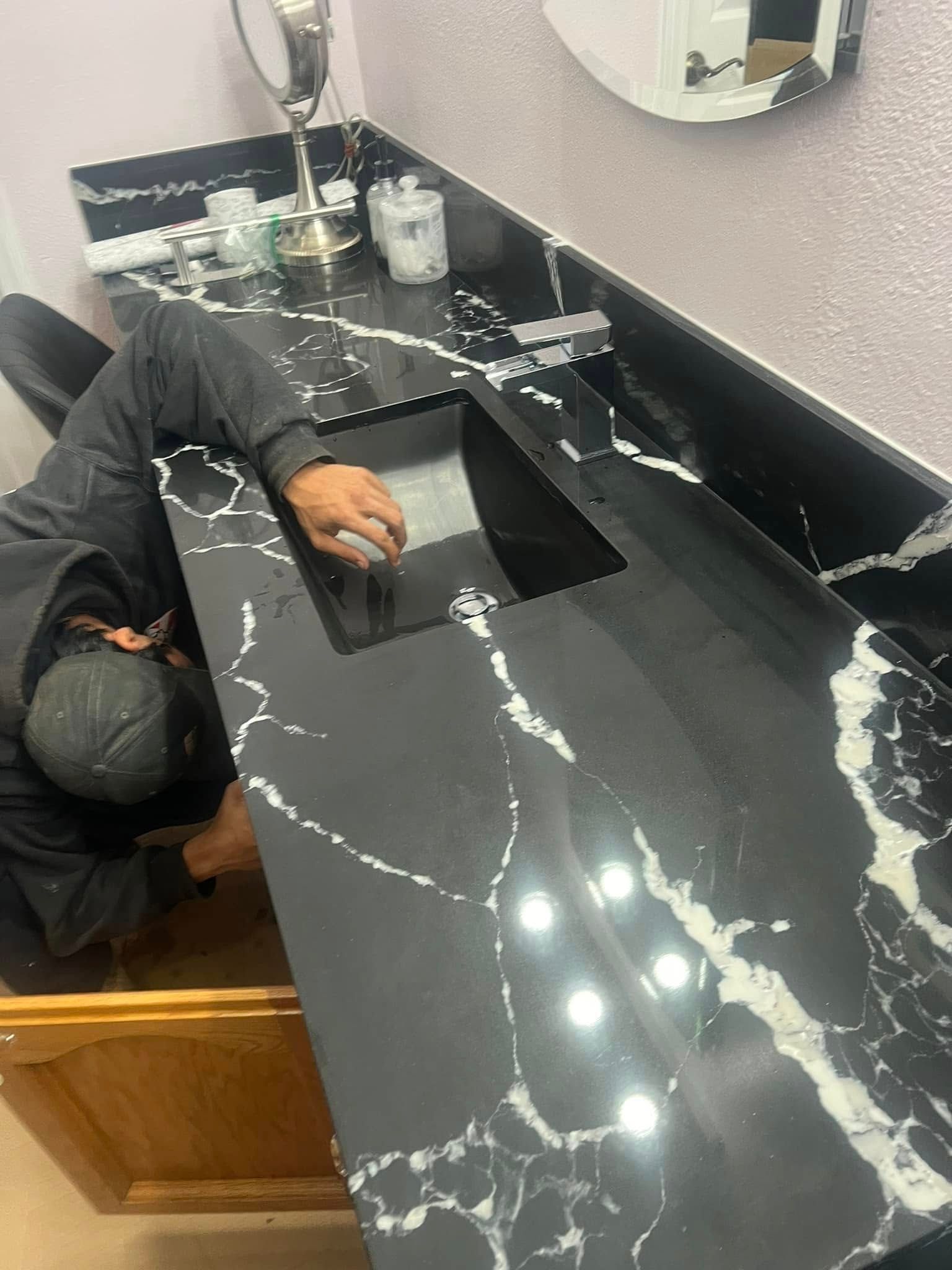 Person installing a black marble countertop with white veining in a bathroom.