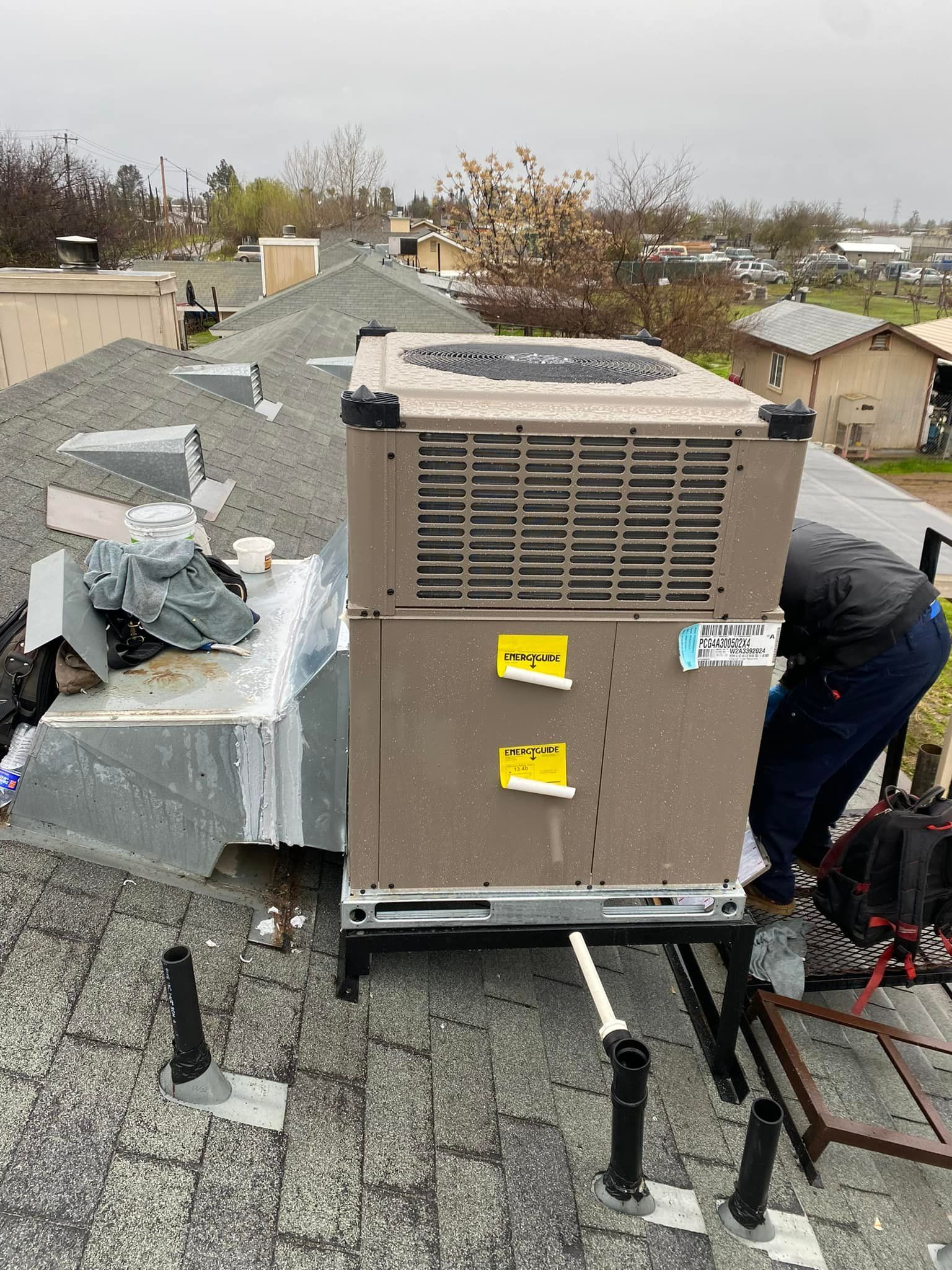 HVAC unit on a rooftop being serviced by a person in blue jeans.