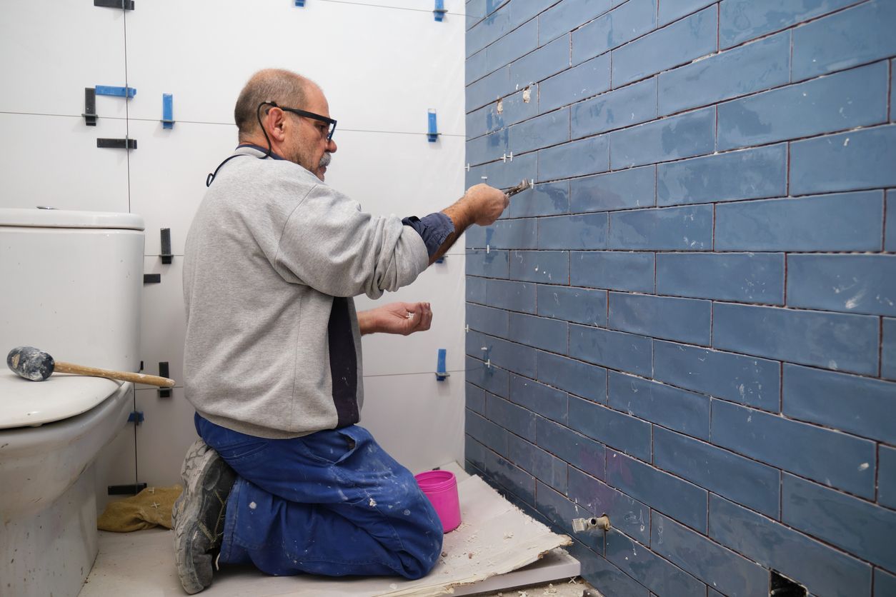 Senior constructor worker removing the separation between tiles on the wall for a bathroom upgrade