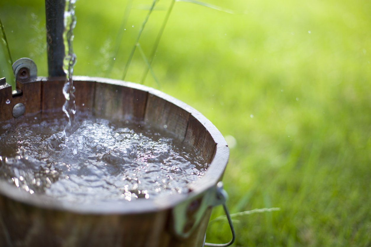 owning your own water well;Fresh water from a well flows out into an old bucket.