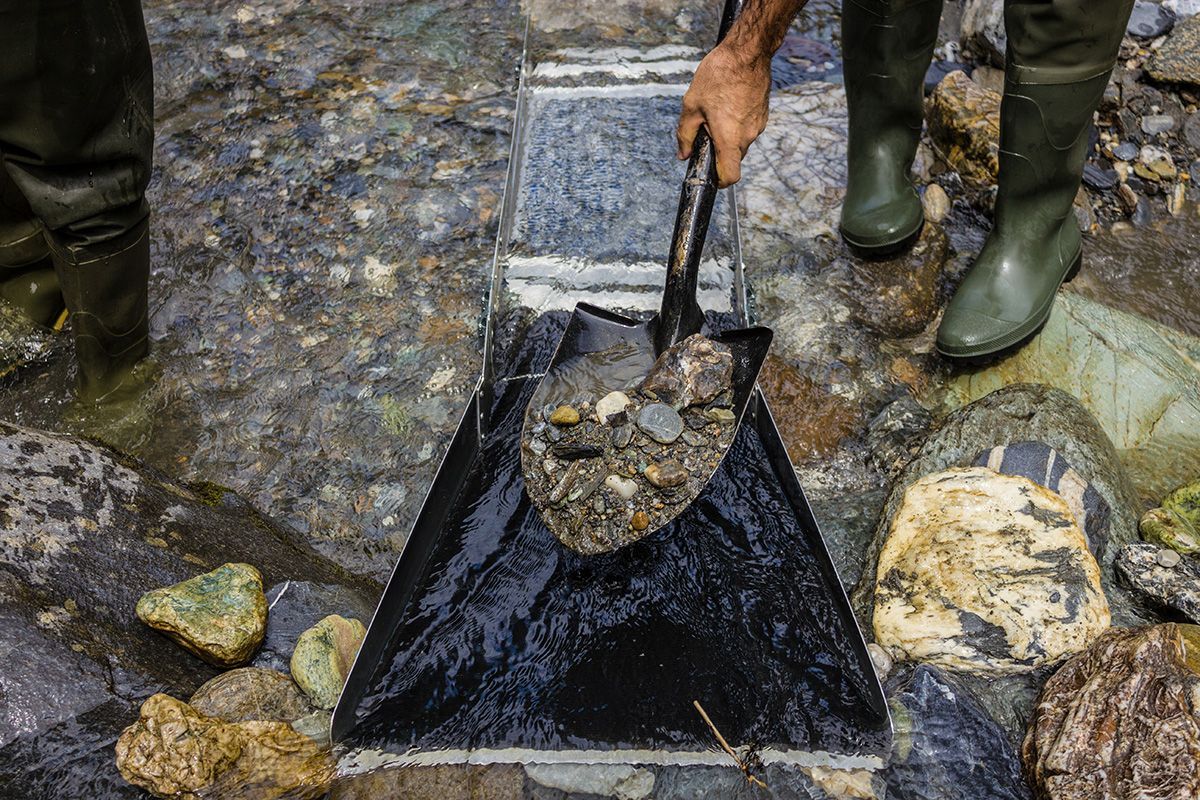 A person is holding a shovel over a bag of rocks.