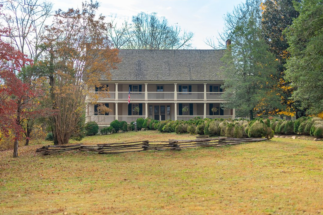 A large house with a porch is surrounded by trees and grass.