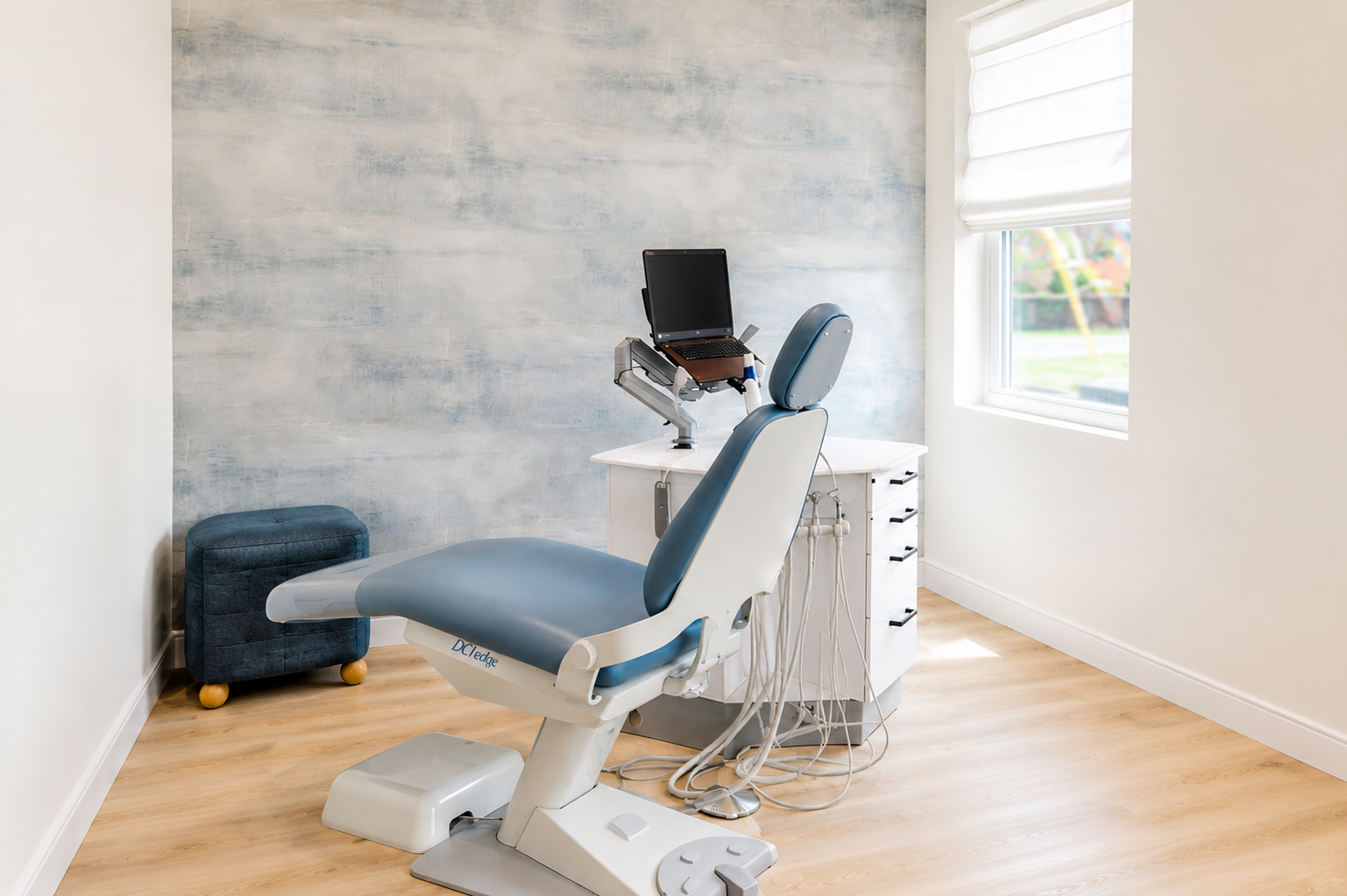 Medical exam room with an exam chair, computer station, and bright window.