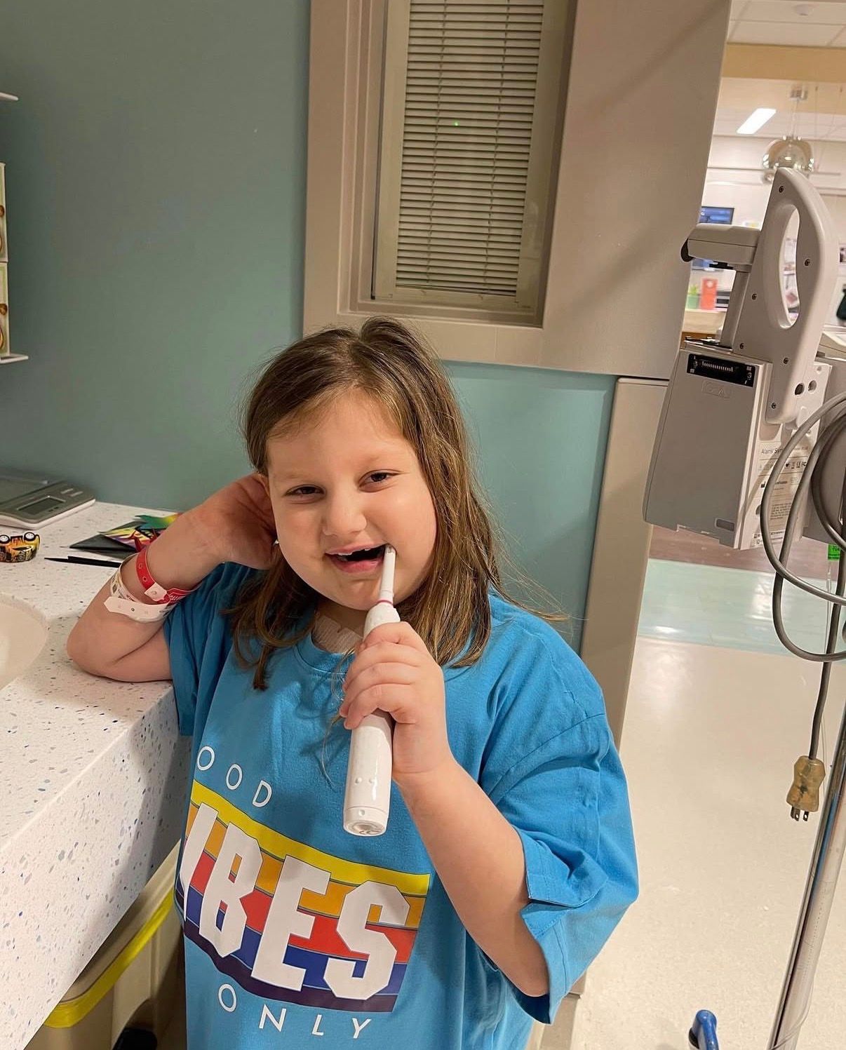 Child in a blue shirt smiling and holding a microphone in a hospital hallway