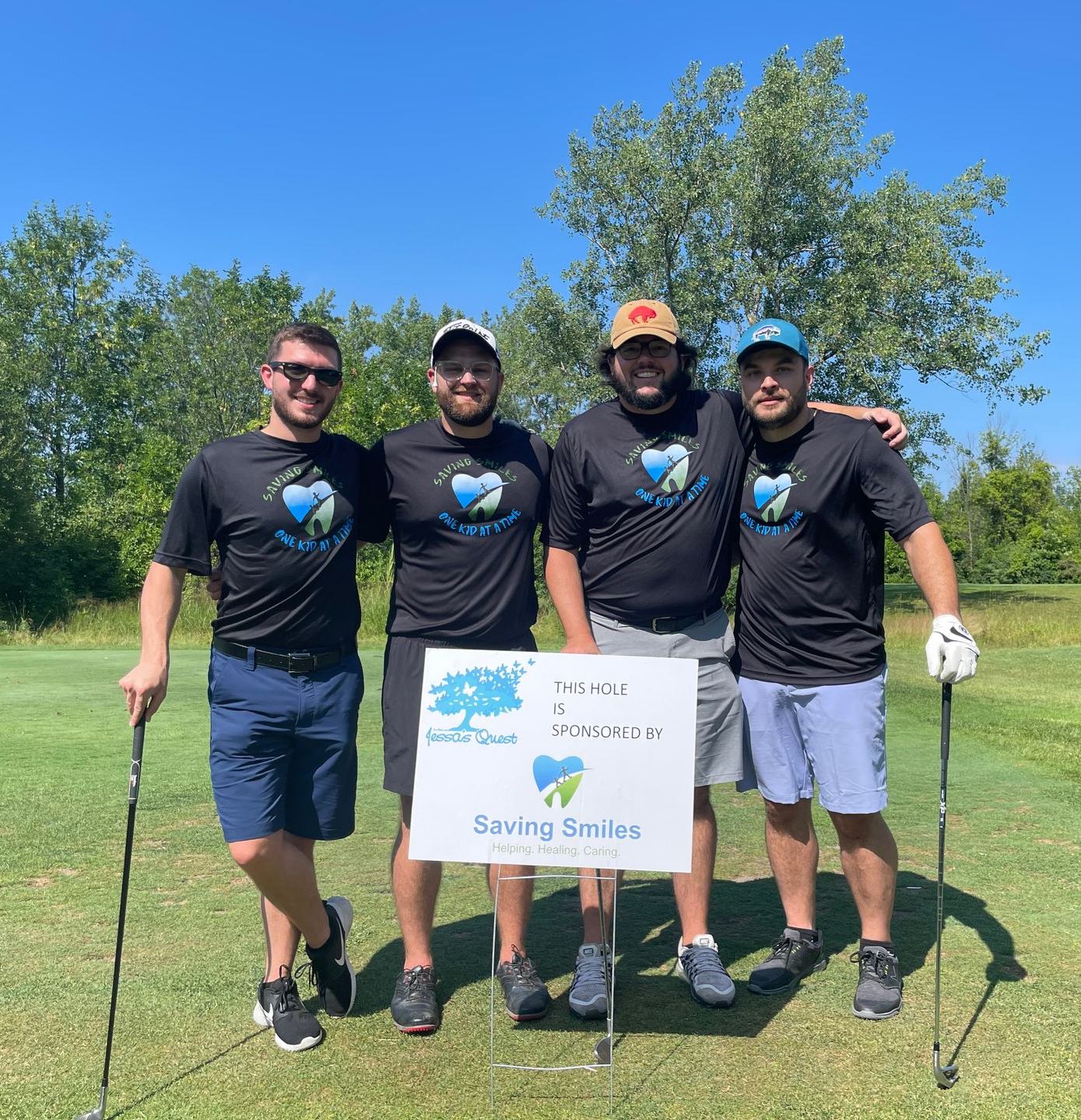 Four golfers in matching black shirts holding a “Saving Selkirk” sign on a sunny golf course