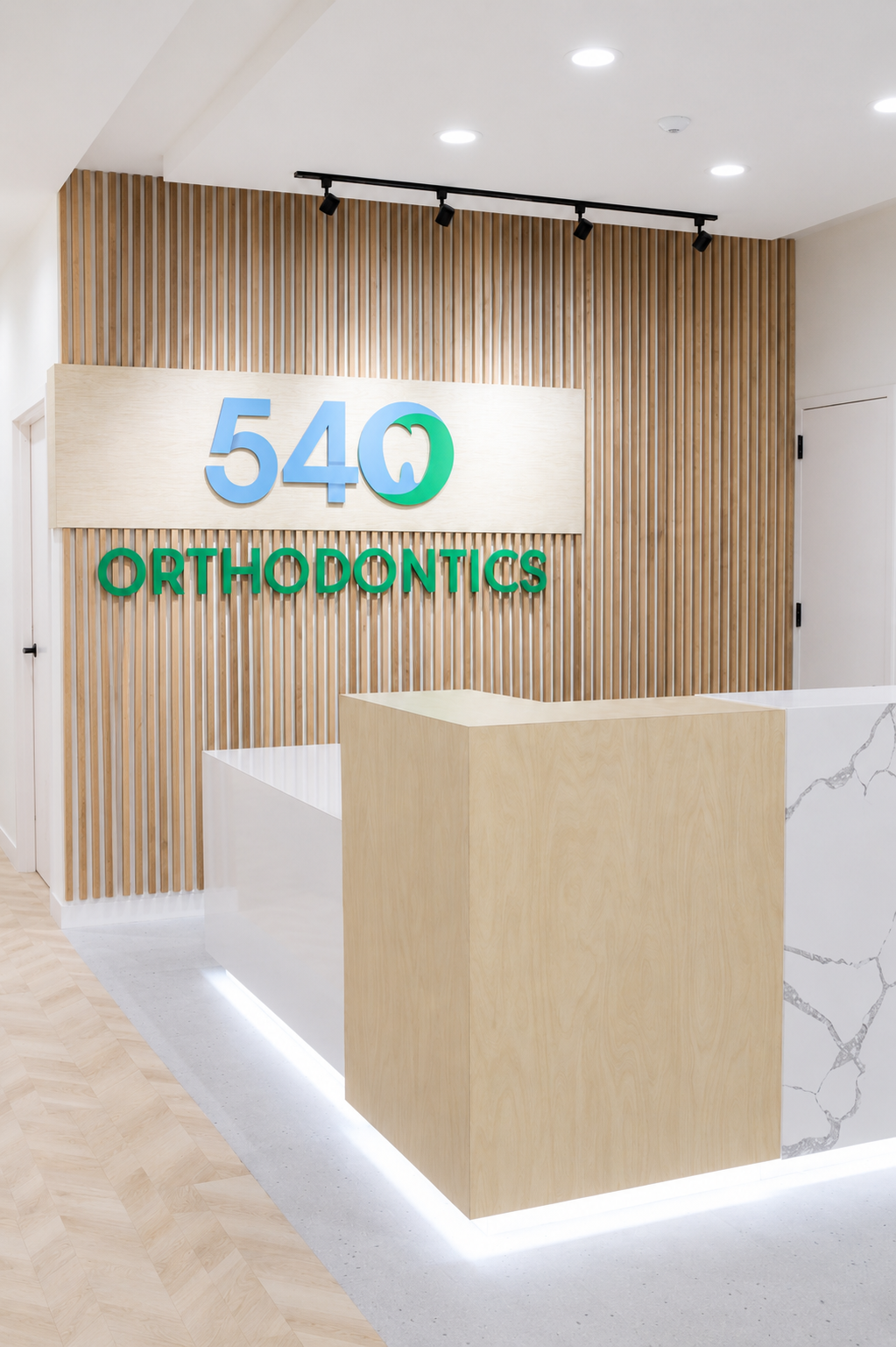 540 Orthodontics reception desk with wood slat wall, white counters, and soft LED lighting