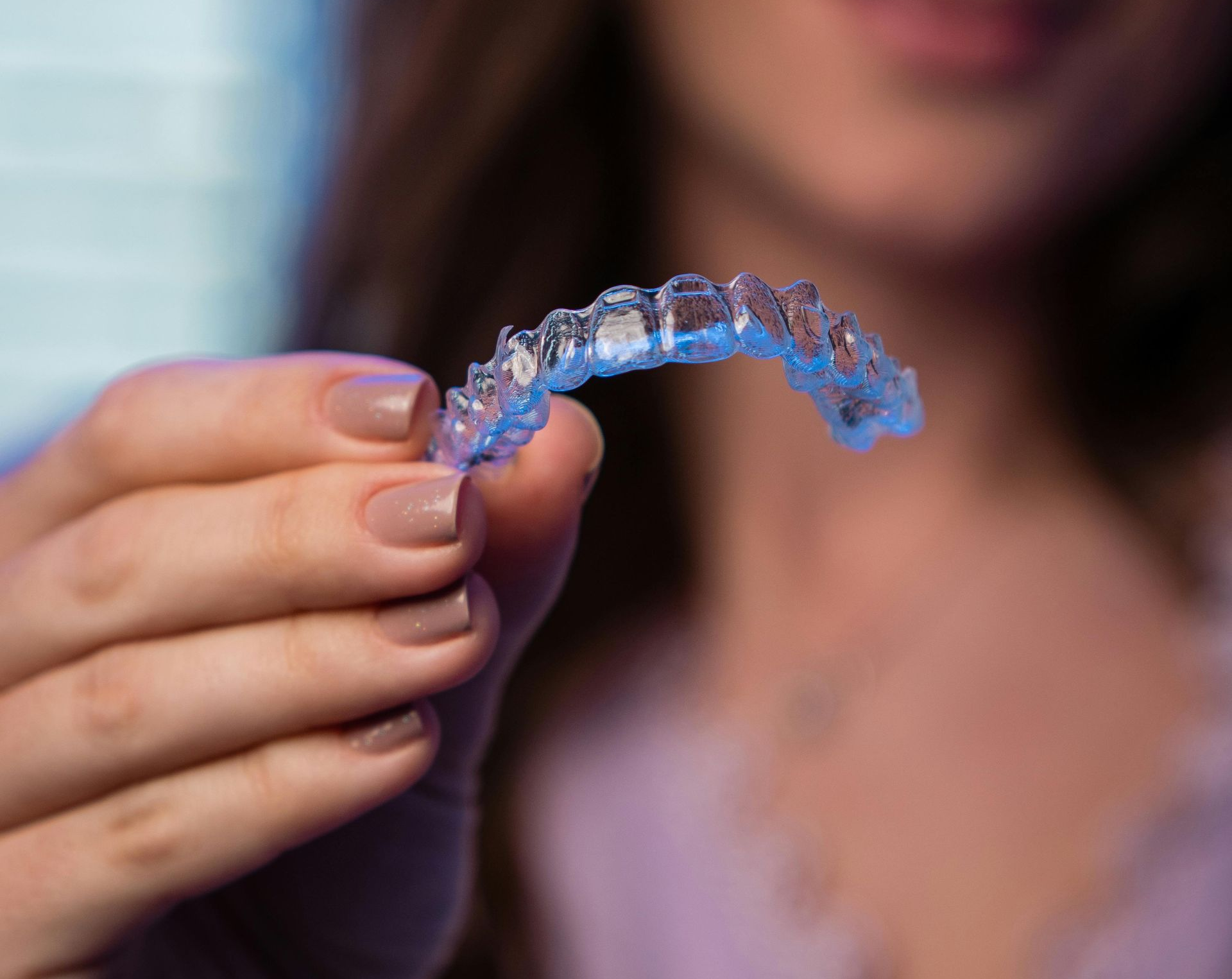Hand holding a clear dental aligner close to the camera