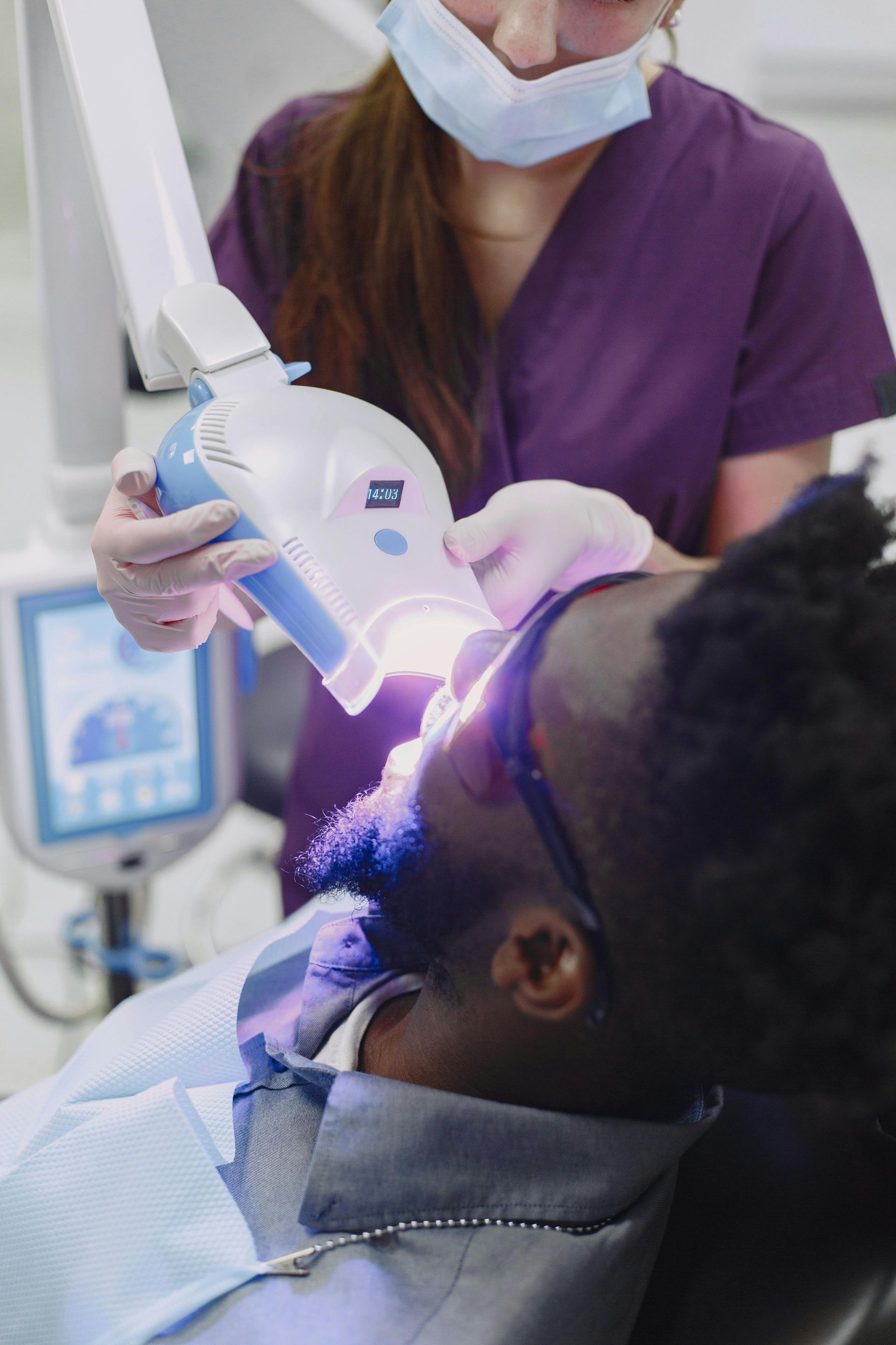 Dentist using a blue curing light on a patient’s mouth during dental treatment