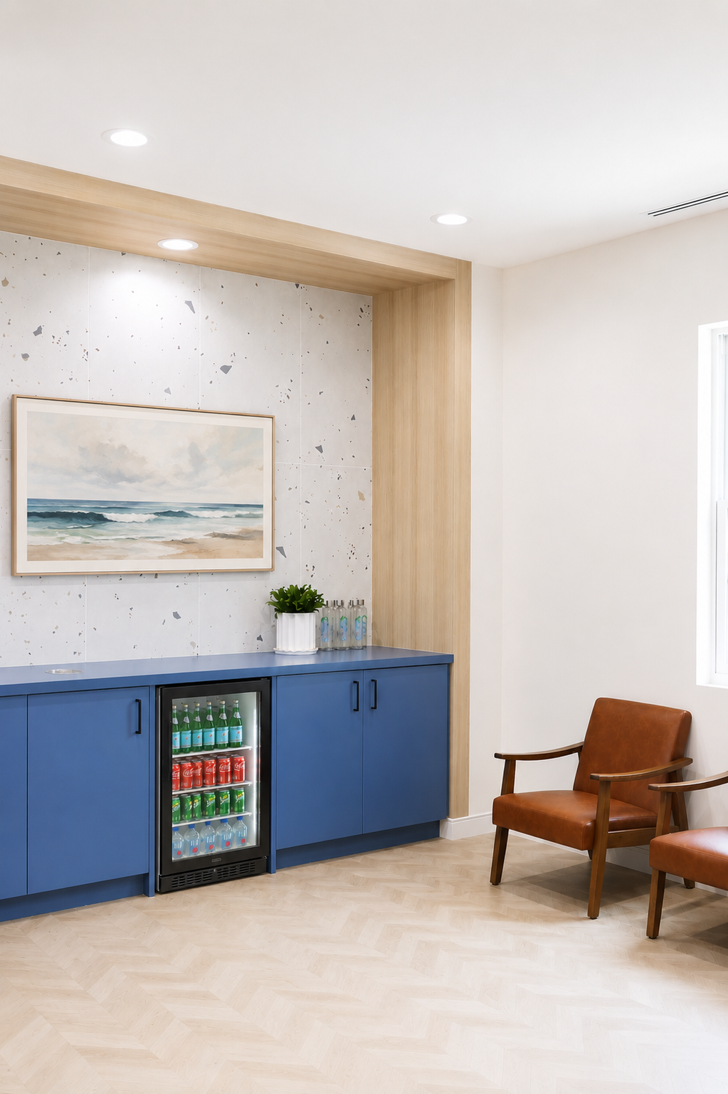 Modern waiting room with blue cabinets, framed artwork, mini fridge, and two wooden chairs.
