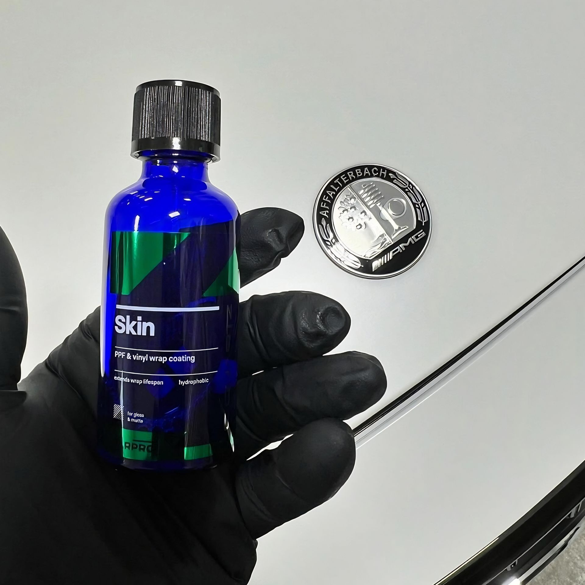 Gloved hand holding a blue bottle labeled “Skin” beside a small round tin on a light surface