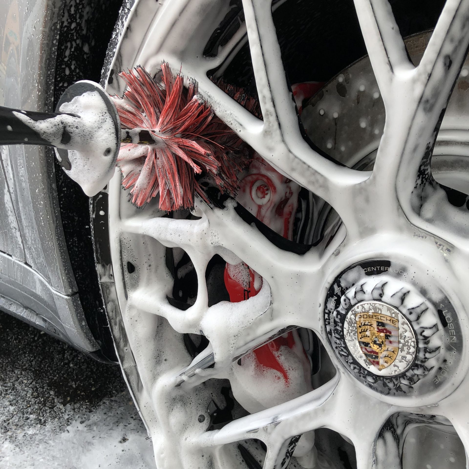 Close-up of a car wheel being washed with white foam and a red brush