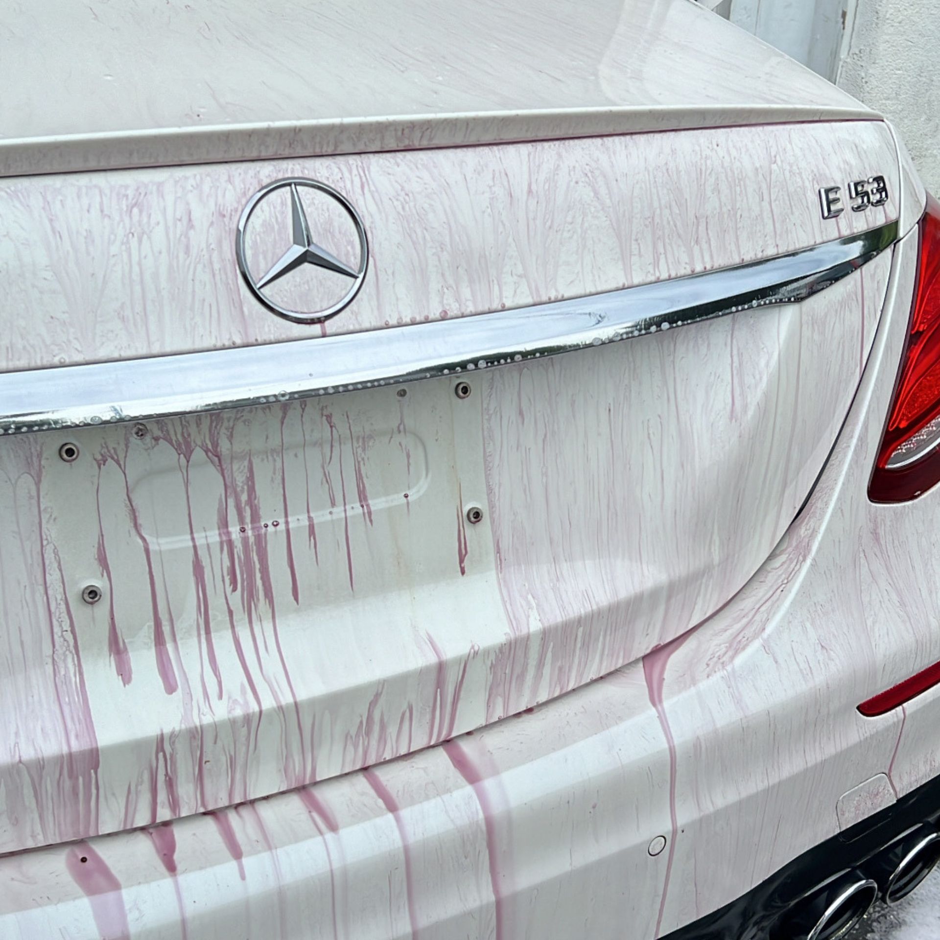 Rear of a white Mercedes sedan with red paint streaks and a small dent on the trunk lid