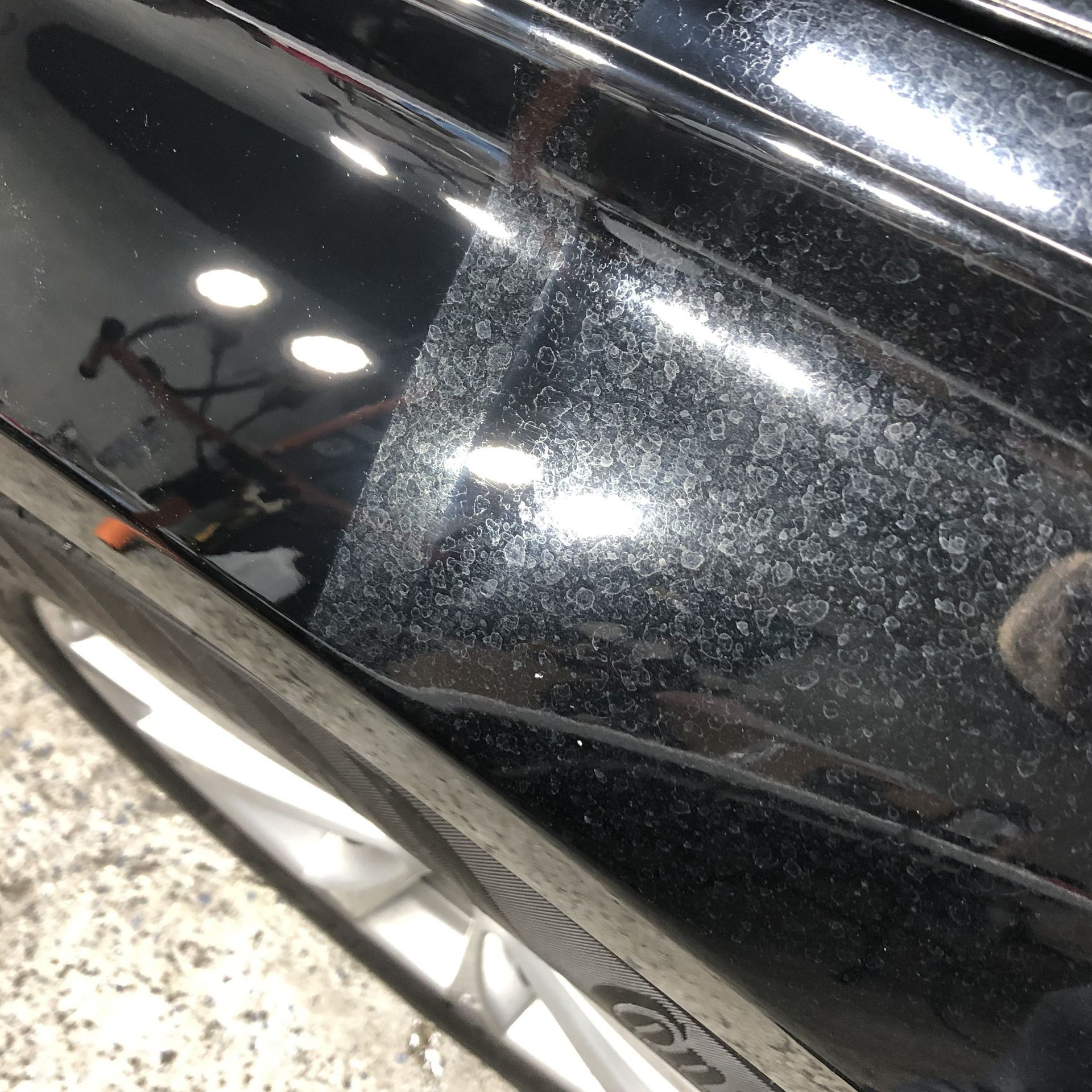 Close-up of a black glossy vehicle panel with bright reflections and dust specks