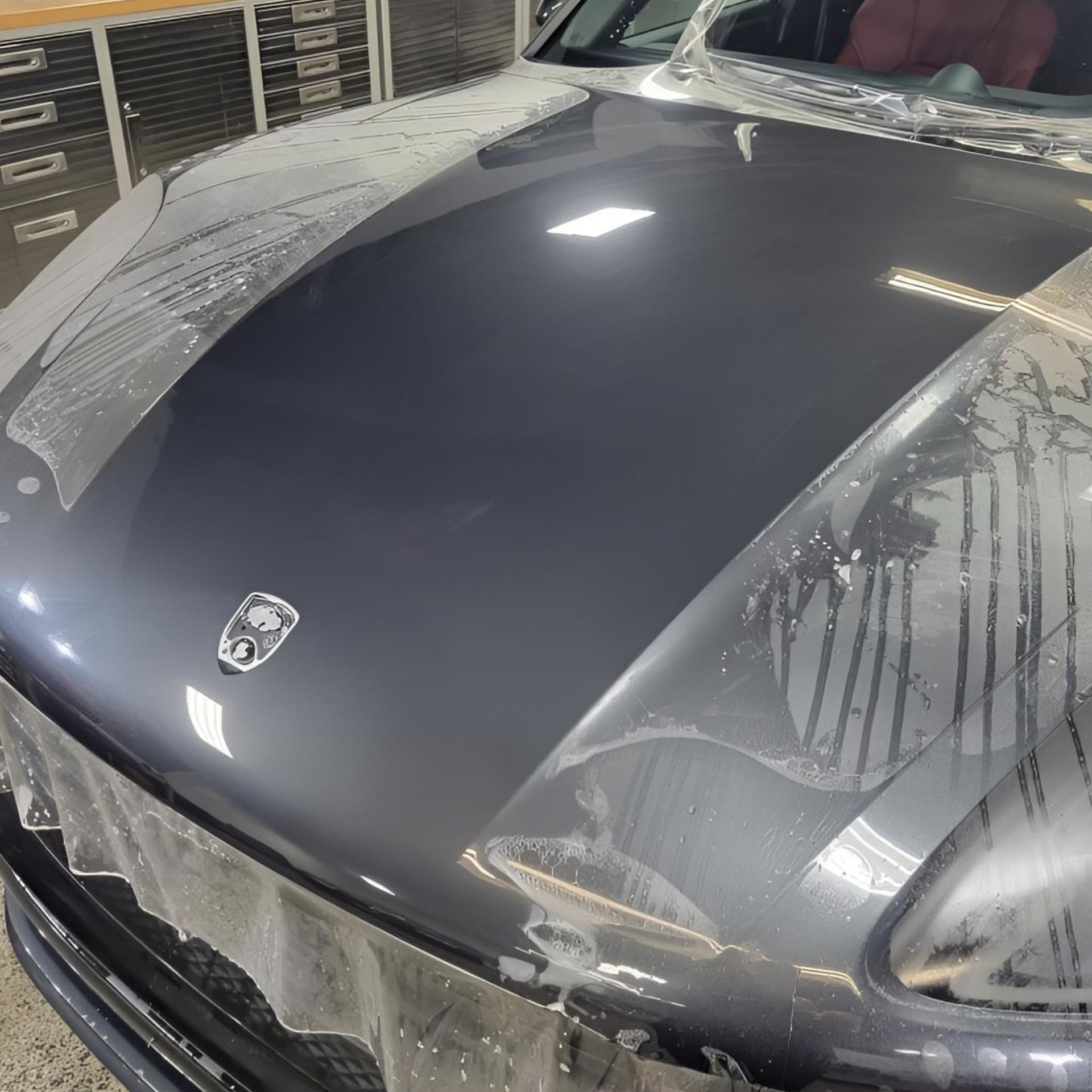 Dark gray car hood partially wrapped in clear protective film inside a garage