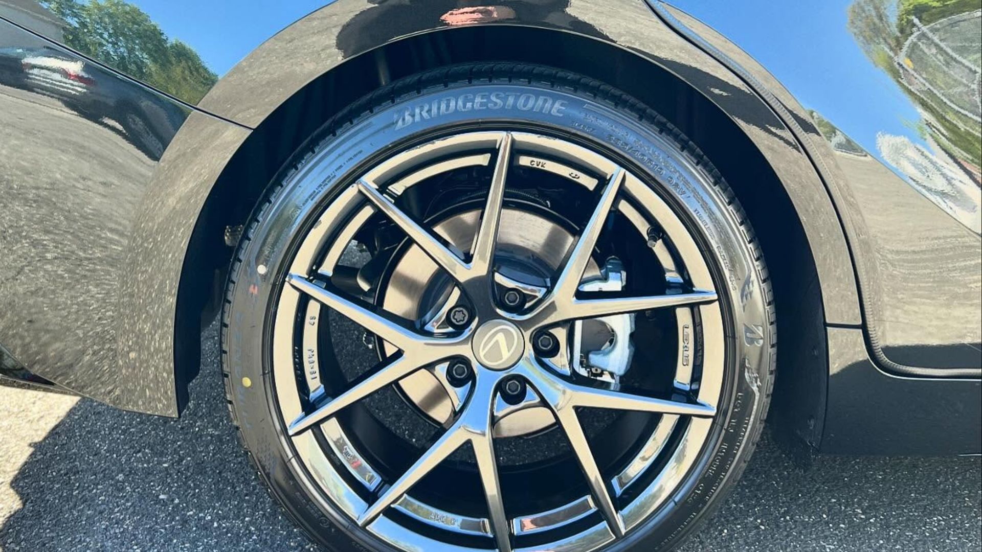 Close-up of a black-and-silver car wheel and tire on a sunlit road