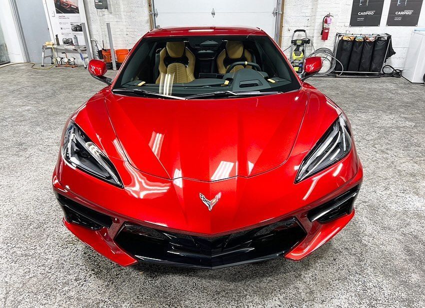 Red Chevrolet Corvette parked indoors, front view in a garage with tan interior visible.