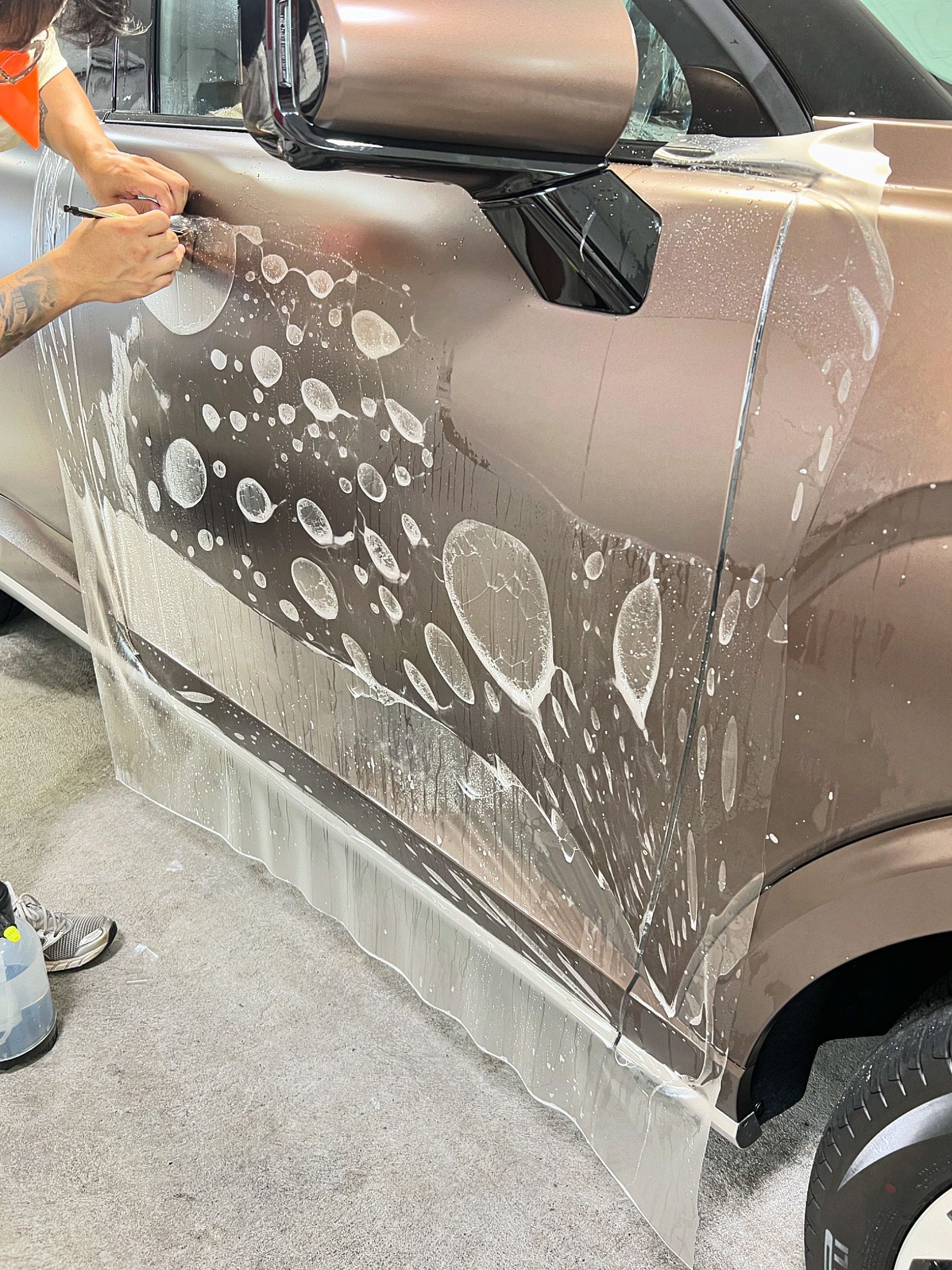 Person washing a gray car with soap suds at a car wash