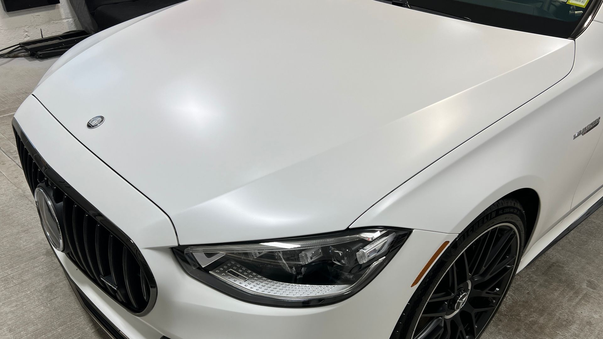 White luxury sedan front corner with black grille and headlights in a garage