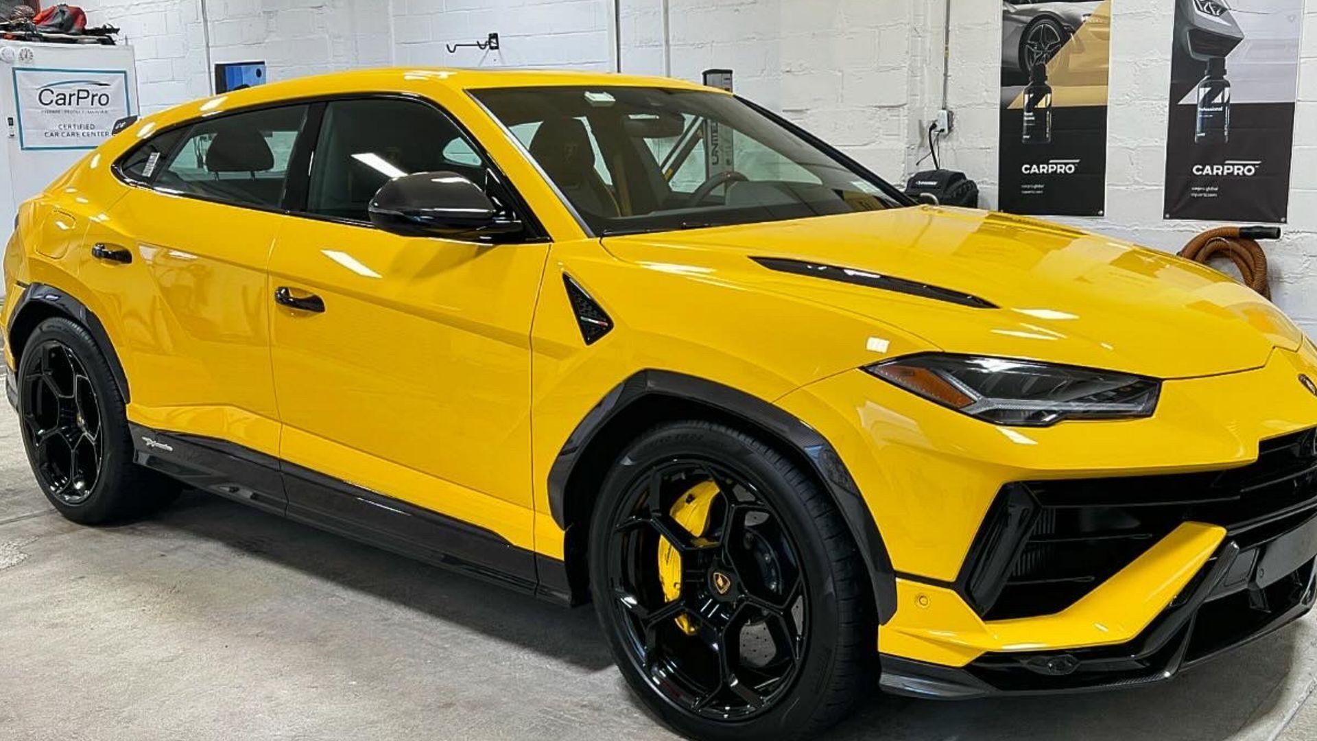Yellow Lamborghini Urus SUV parked indoors in a garage, with black wheels and trim.