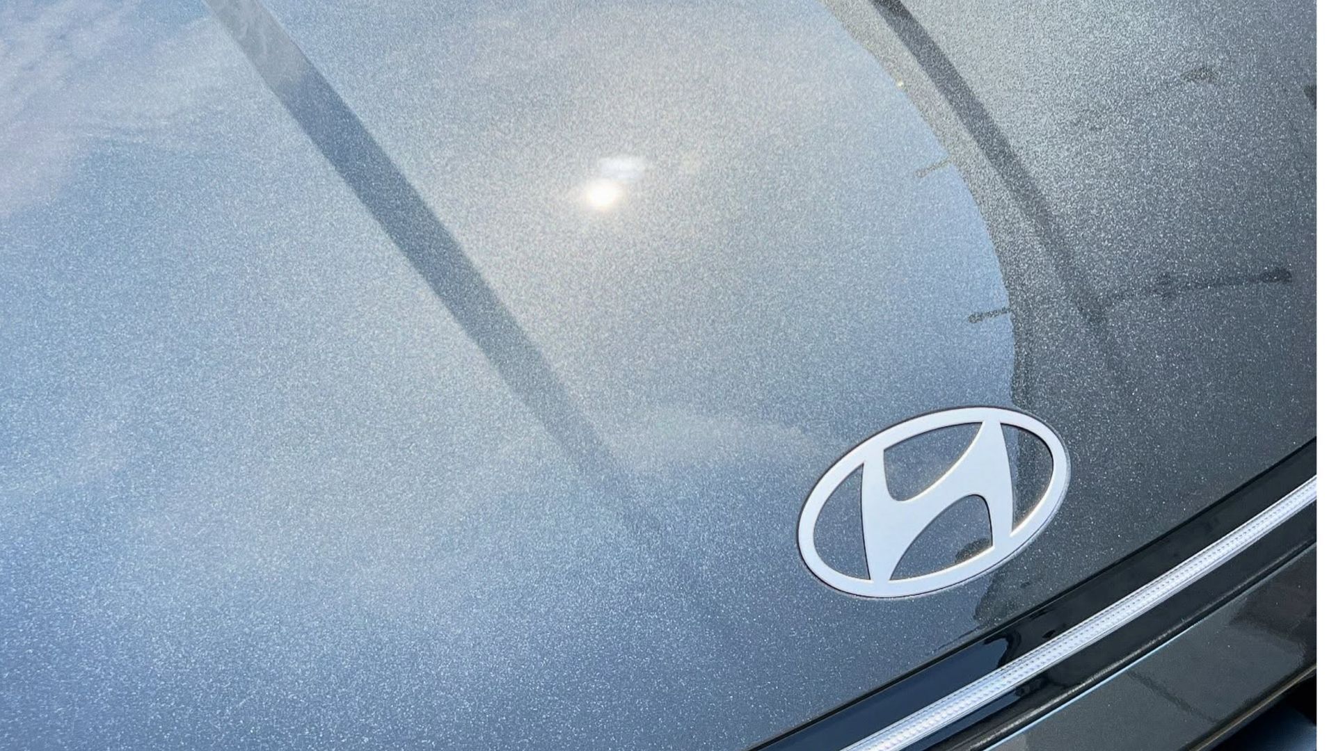 Close-up of a silver Hyundai car hood with water droplets and the Hyundai logo.