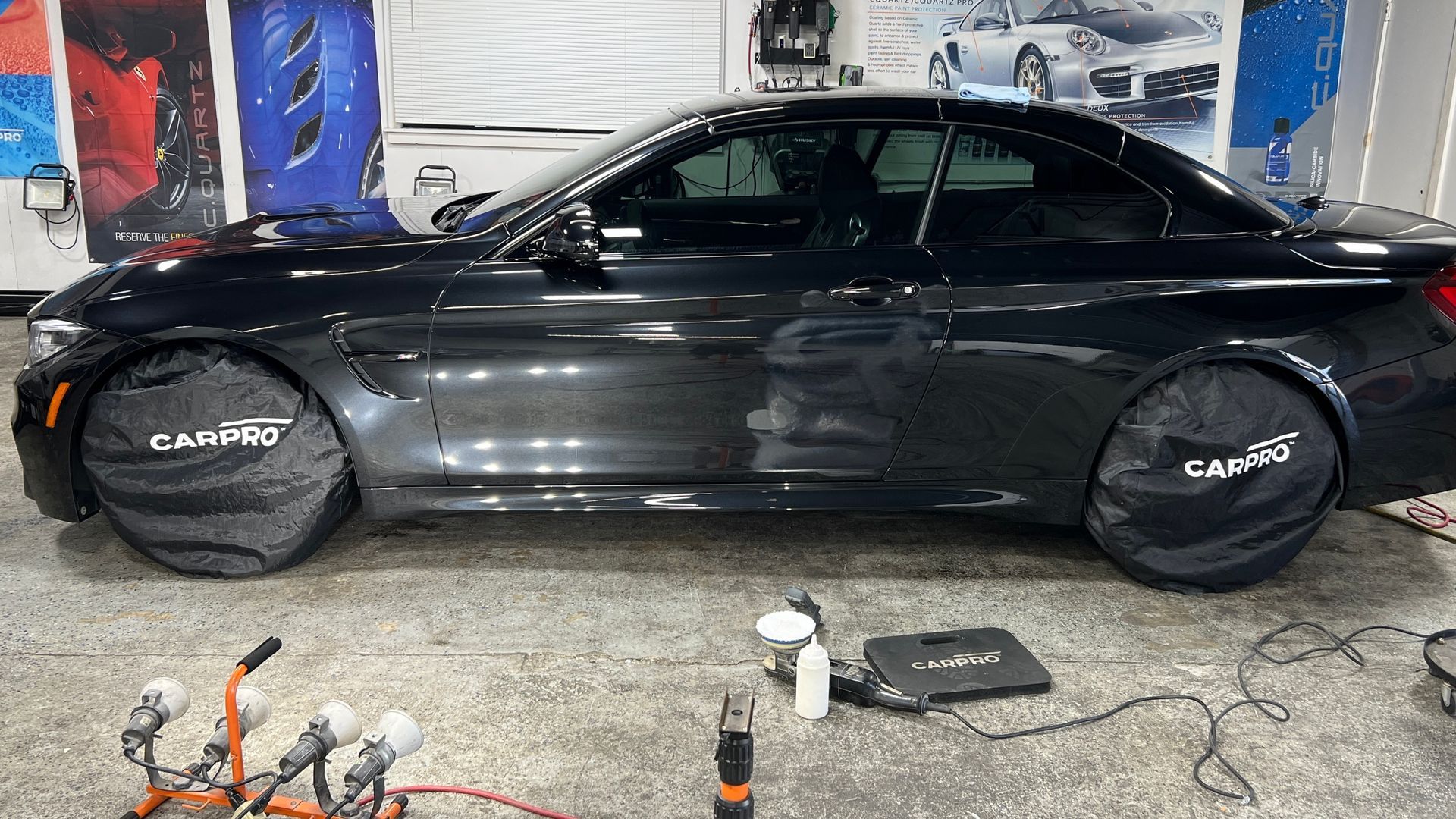 Black sedan in an auto shop with wheel covers on, surrounded by tools and equipment.