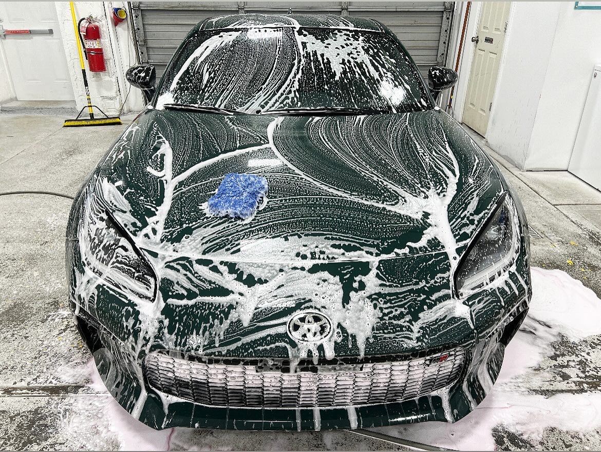 Dark green sports car covered in white soap suds in a garage