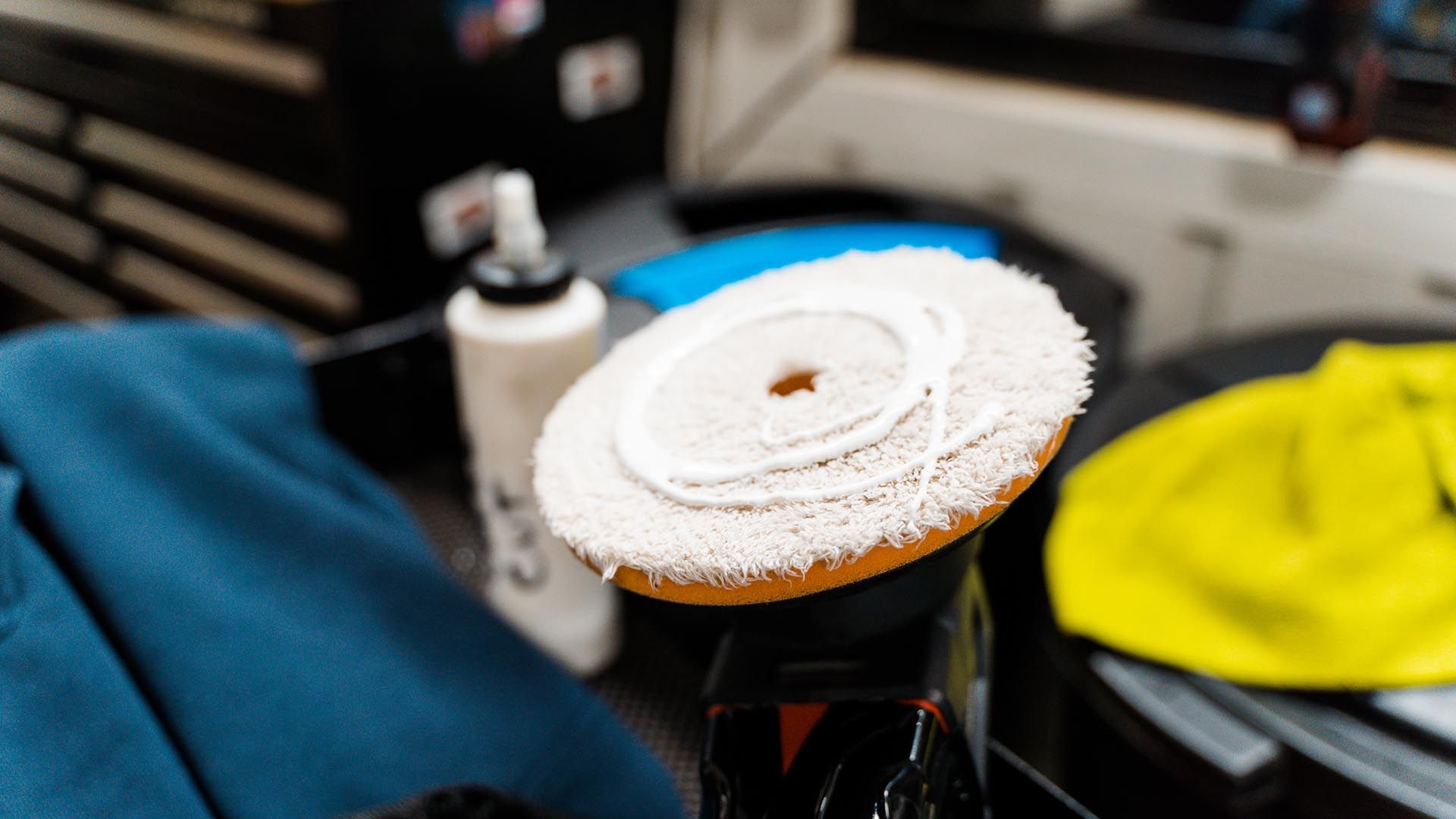 Automotive buffer pad with white polishing pad on a workbench, surrounded by towels and supplies