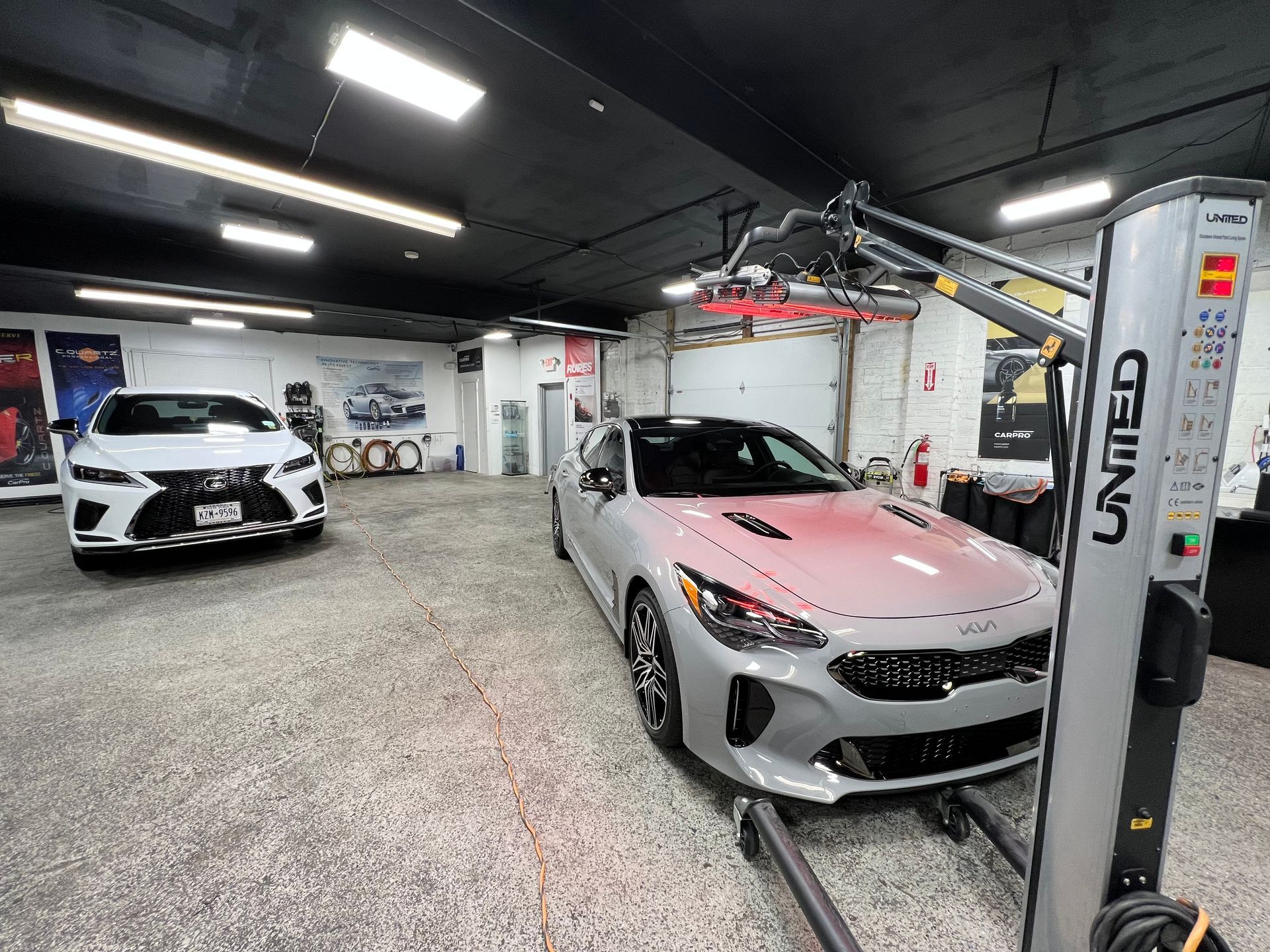 Luxury car showroom with a silver sports car under a ceiling lift and a white car in the background
