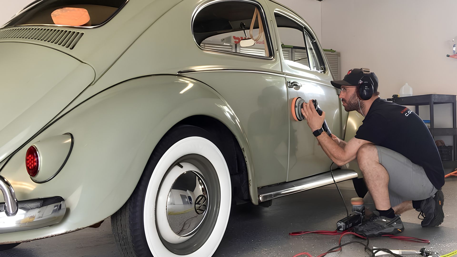 Man using a buffer to polish a vintage gray Volkswagen Beetle in a garage