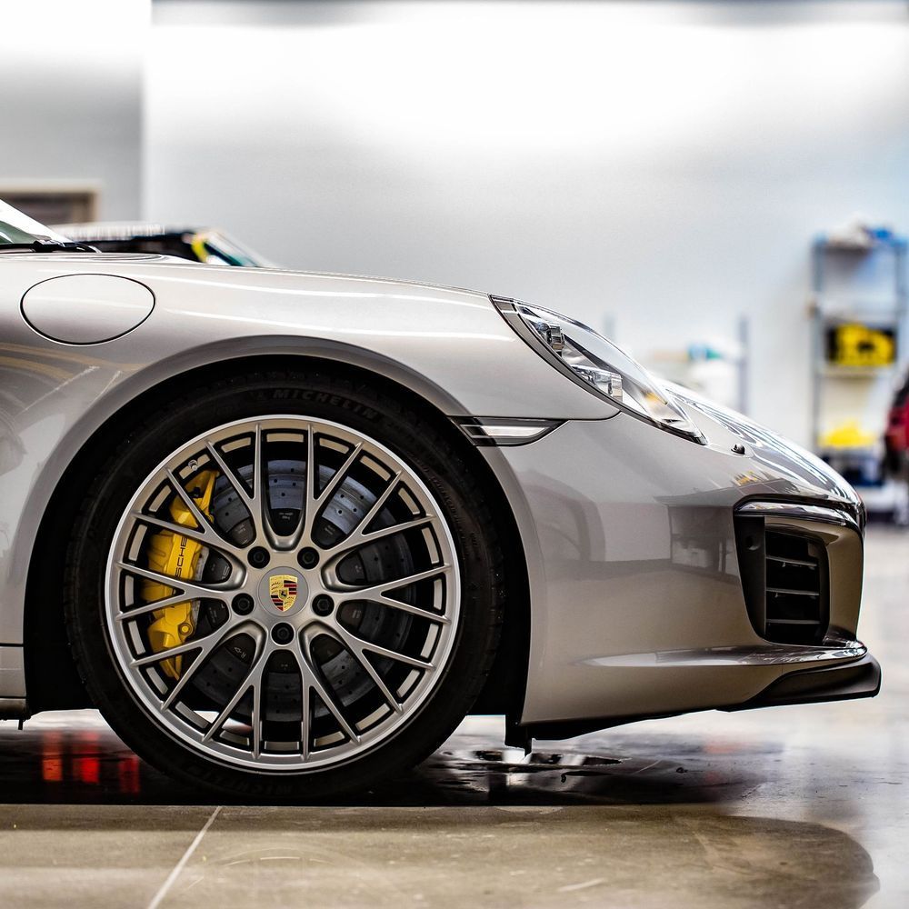 Silver sports car front wheel and bumper in a garage, with large alloy rim and Porsche badge
